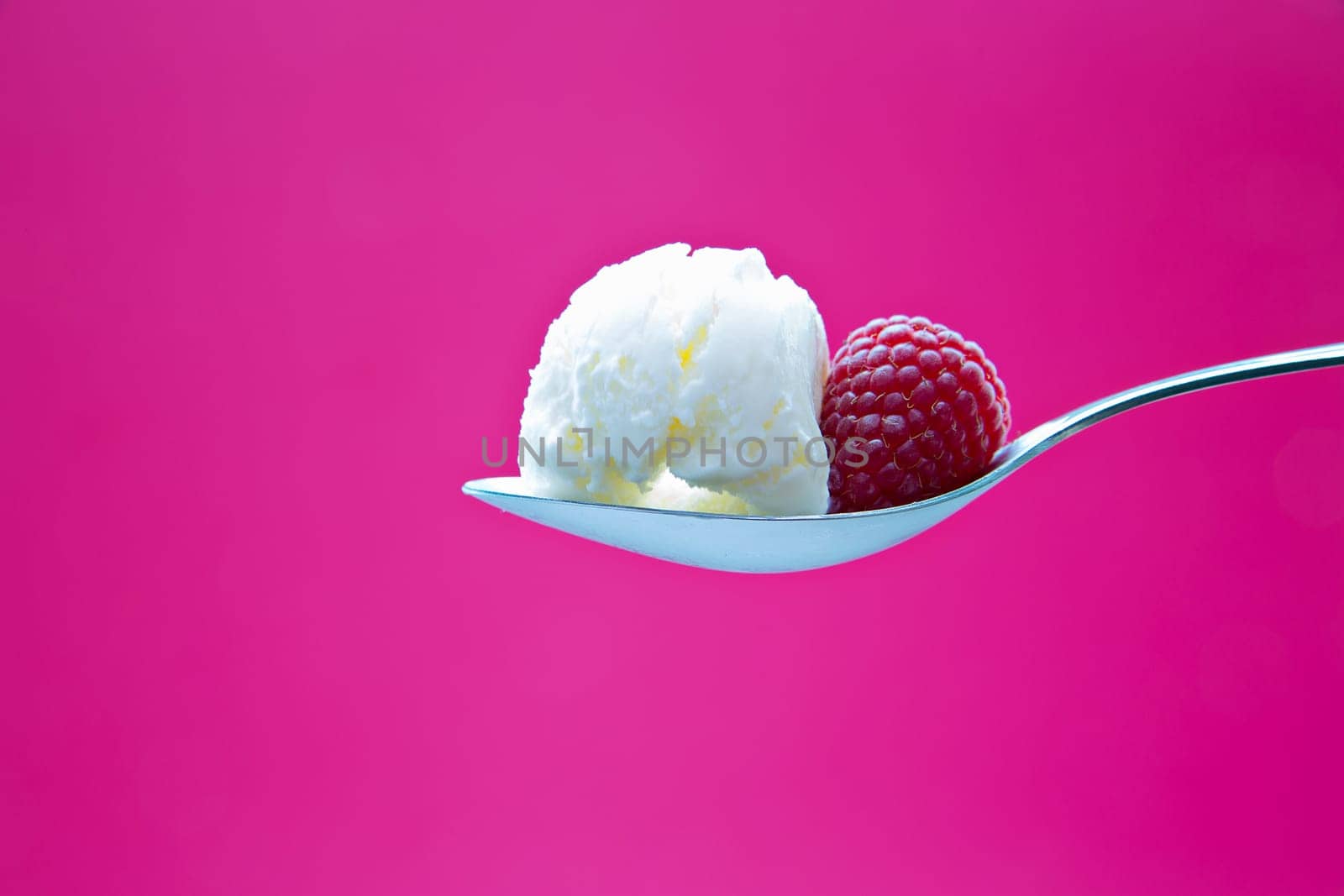 Tasty icecream on metal chromed spoon with raspberry