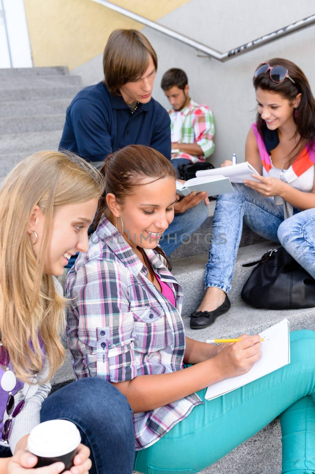 Students sitting on school steps writing studying teens college high-school