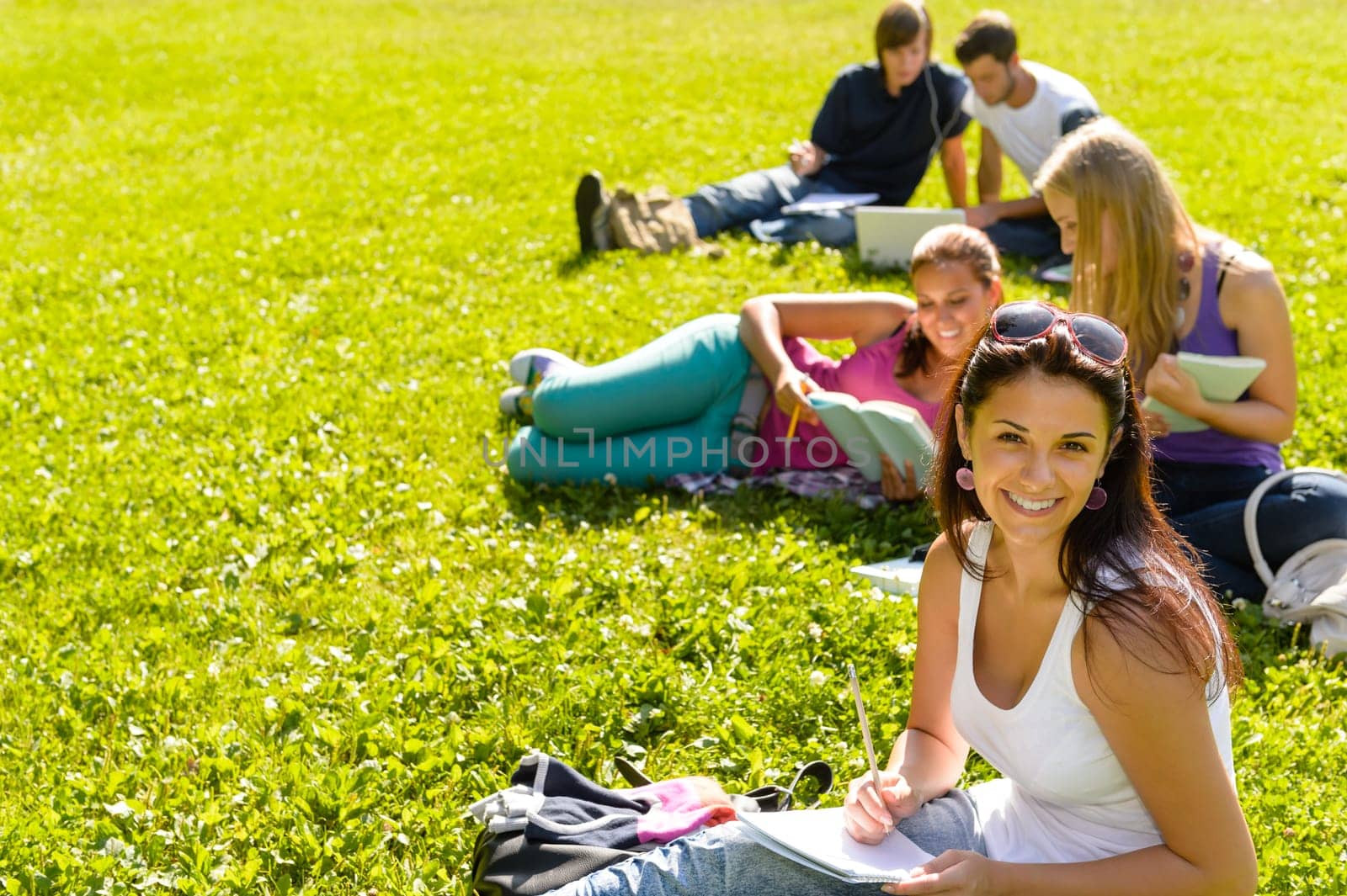 Students studying sitting on grass in park happy teens campus