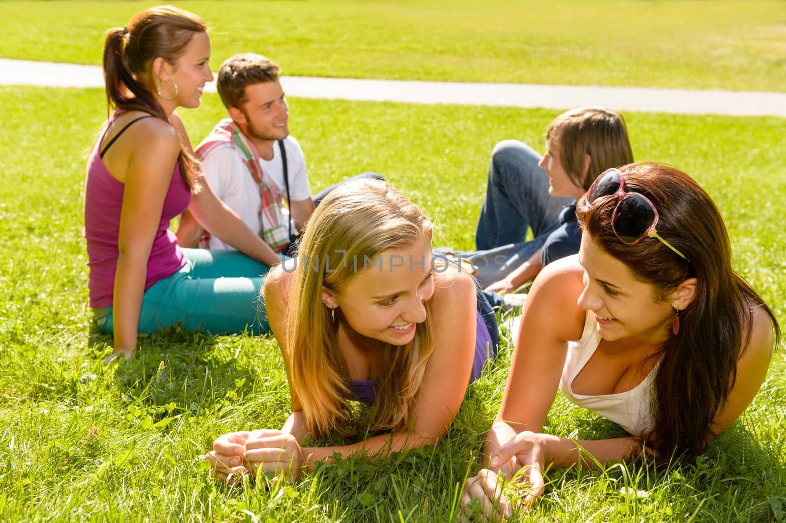 Teens talking relaxing on grass in park happy students friends