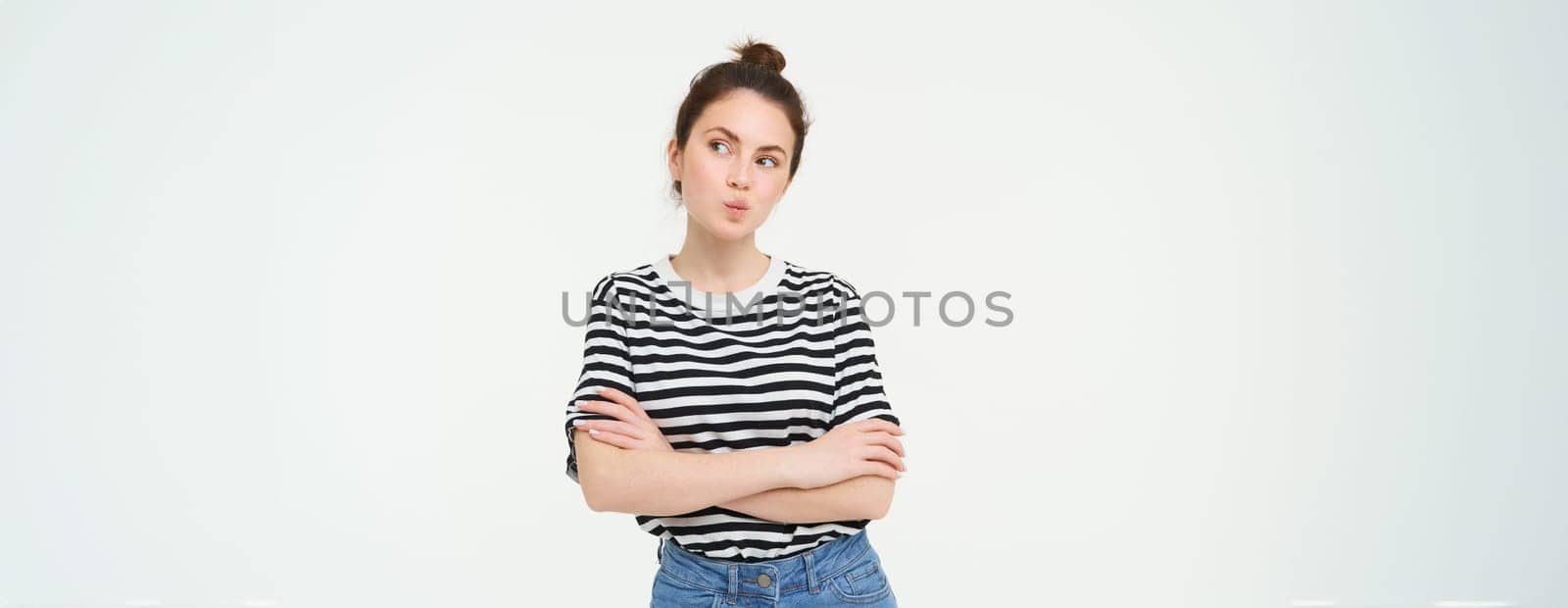 Image of intrigued young woman, thinking, pucker lips with thoughtful face, cross arms on chest, standing over white background.