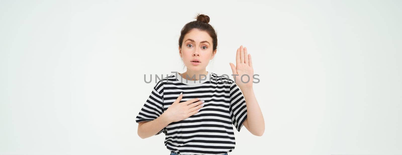 Portrait of honest woman telling truth, makes promise, raising one palm up and holds hand on heart, standing over white background.