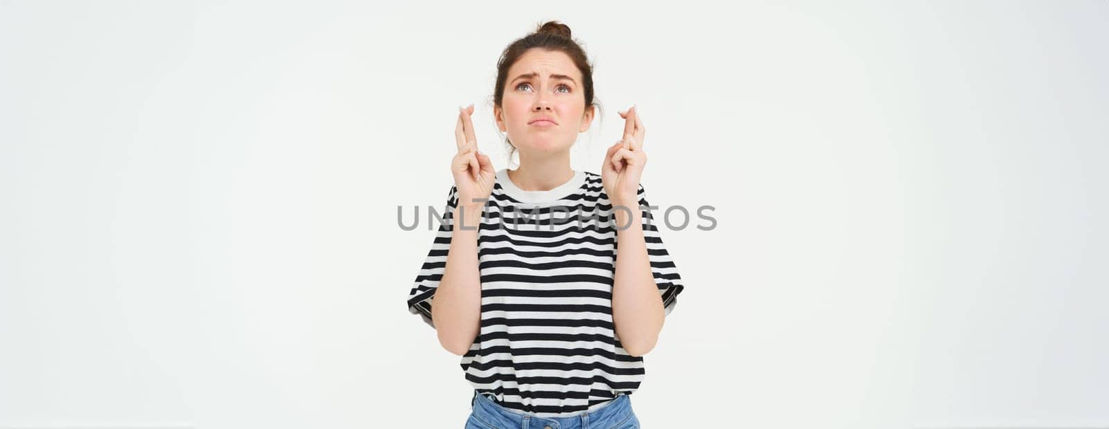 High hopes. Young woman cross fingers, makes wish, anticipates something, stands over white background.