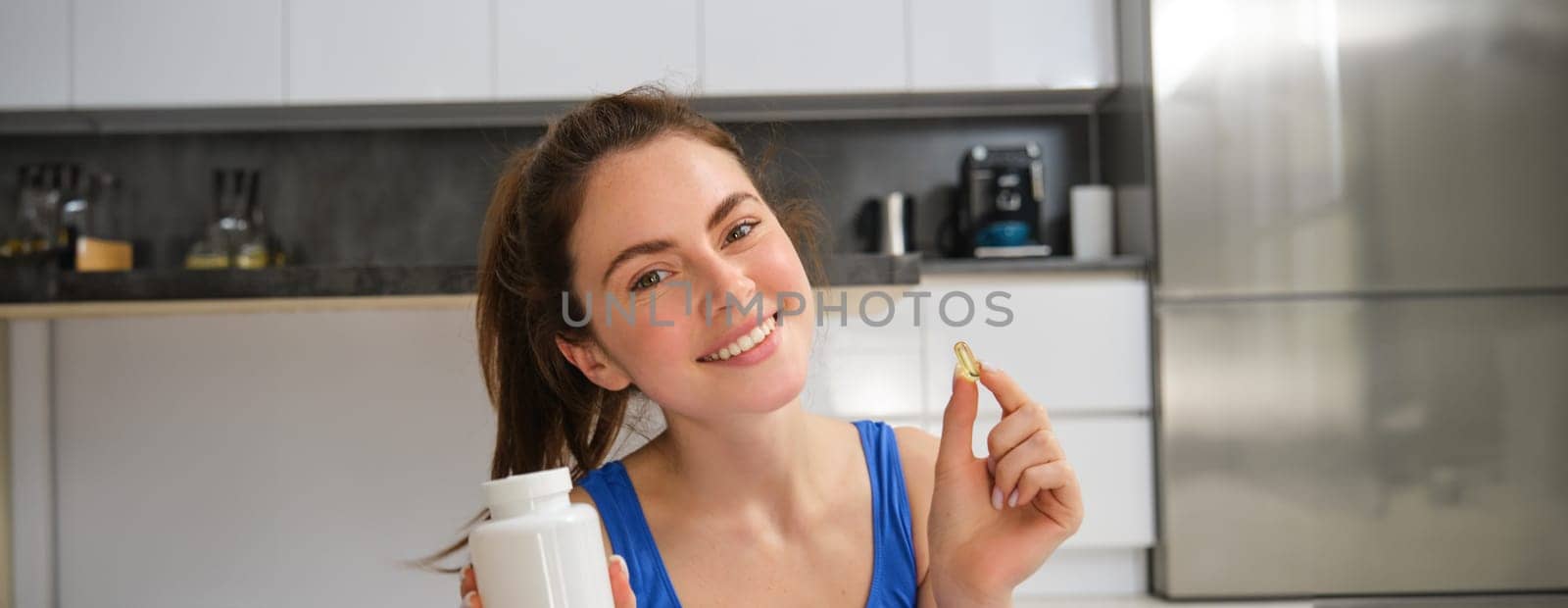 Close up portrait of smiling, healthy young woman, holding tablets, taking vitamin dietary supplements after home fitness workout.