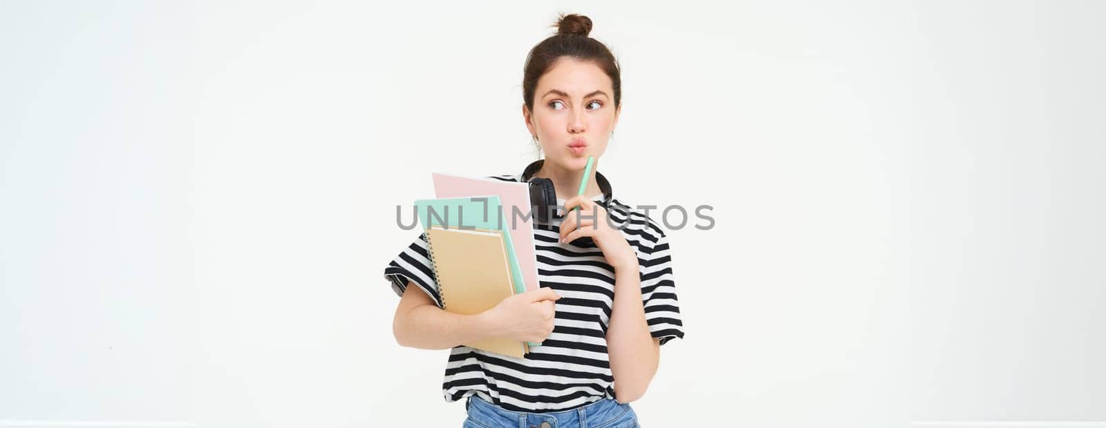 Image of young woman, tutor with books and notebooks, wearing headphones over her neck, isolated on white background. Student lifestyle concept by Benzoix