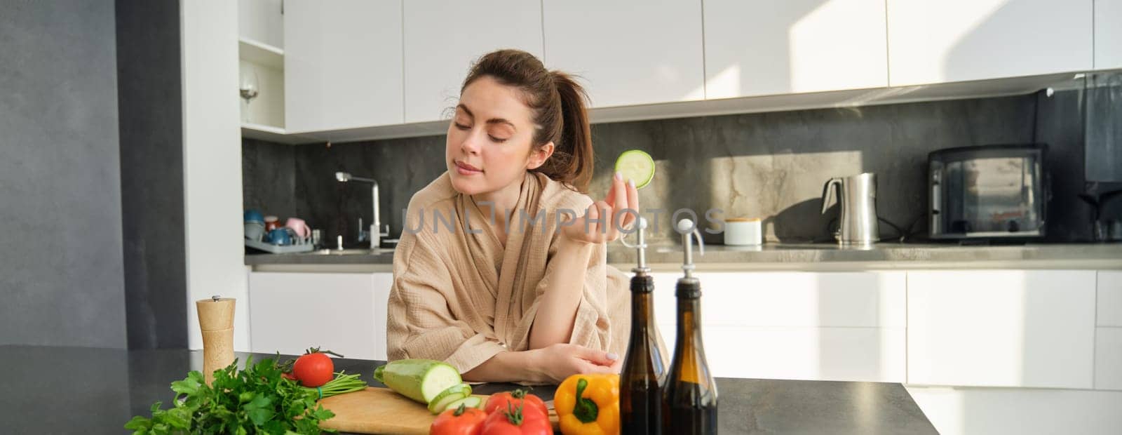 Portrait of brunette woman, wife cooking at home, making dinner, posing near chopping board in kitchen with vegetables, holding zucchini.