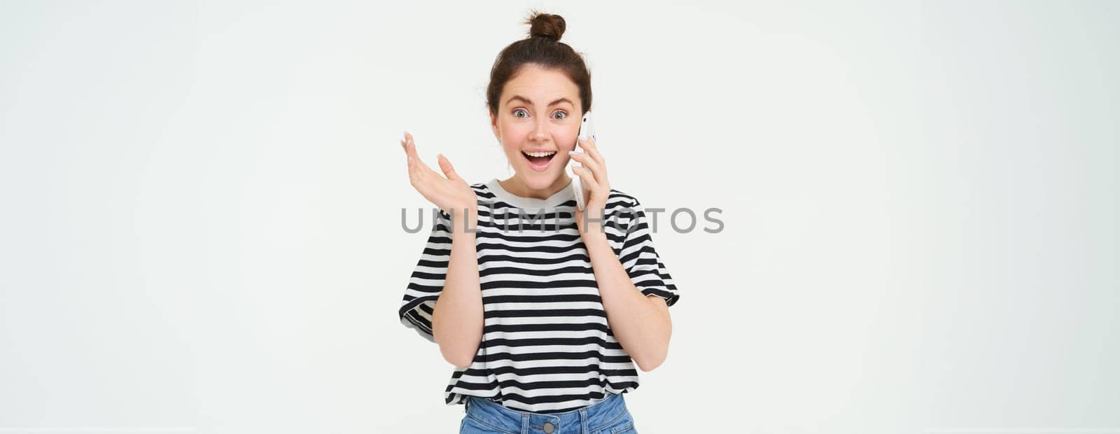 Portrait of girl answers phone call, reacts surprise, stands over white background. Communication and lifestyle concept.