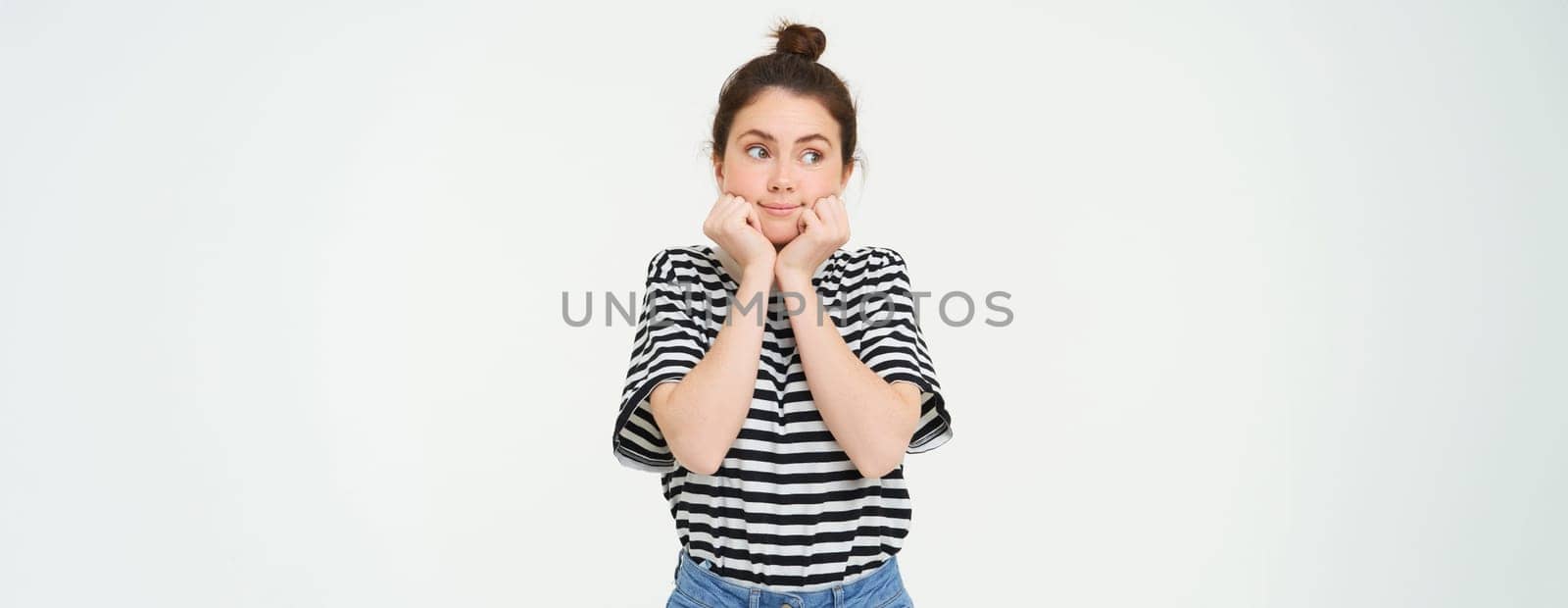 Wellbeing and women concept. Portrait of young woman with cute face, holds hands near head and smiles, isolated against white background.