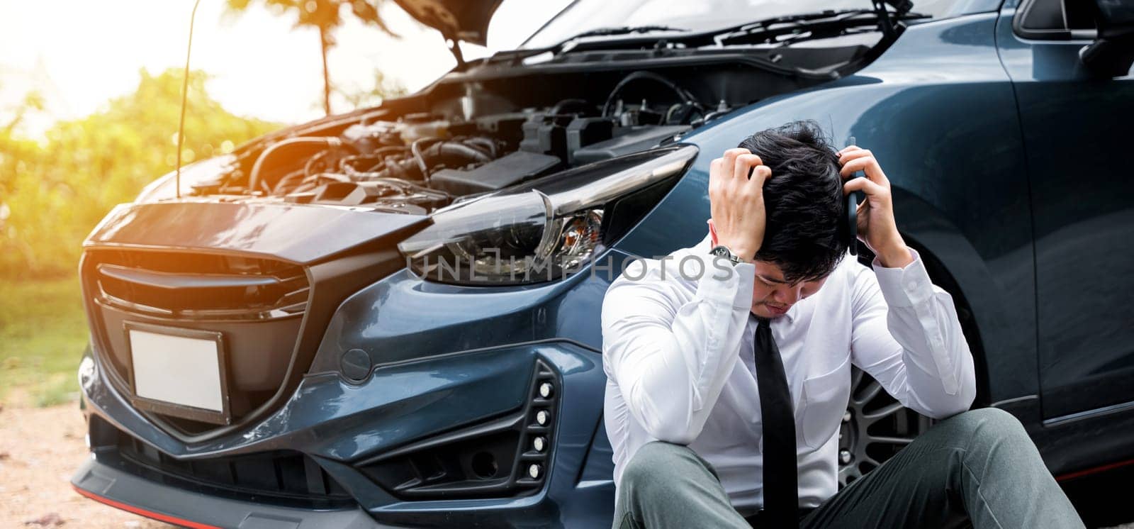 Worried man holding head by hands next to his broken car on rural road, calling for roadside assistance. Concept of car breakdown and frustration.