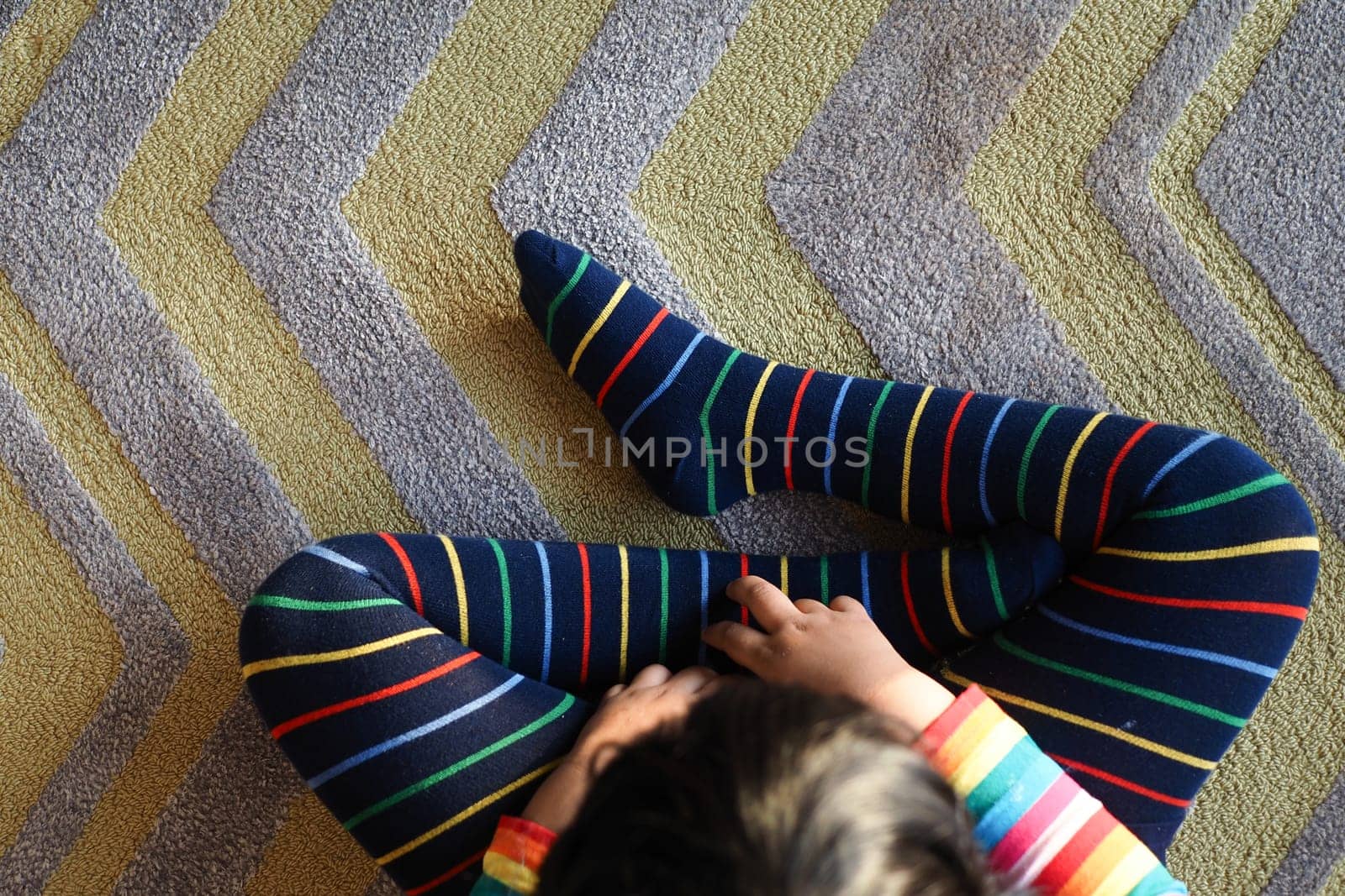 top view of child with Colorful striped socks sitting on carpet ,