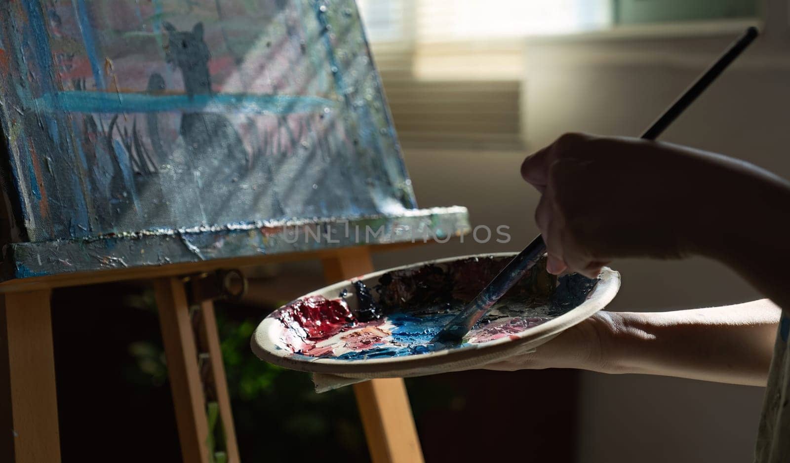 Close-up photo of female artist mixing acrylic paints on a palette. Canvas in the drawing room.