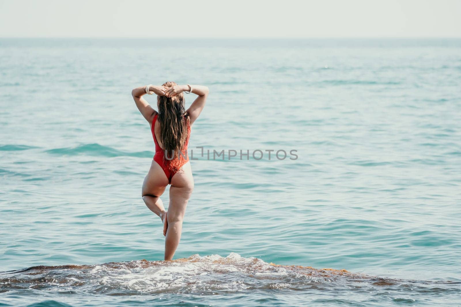 Woman sea yoga. Back view of free calm happy satisfied woman with long hair standing on top rock with yoga position against of sky by the sea. Healthy lifestyle outdoors in nature, fitness concept.