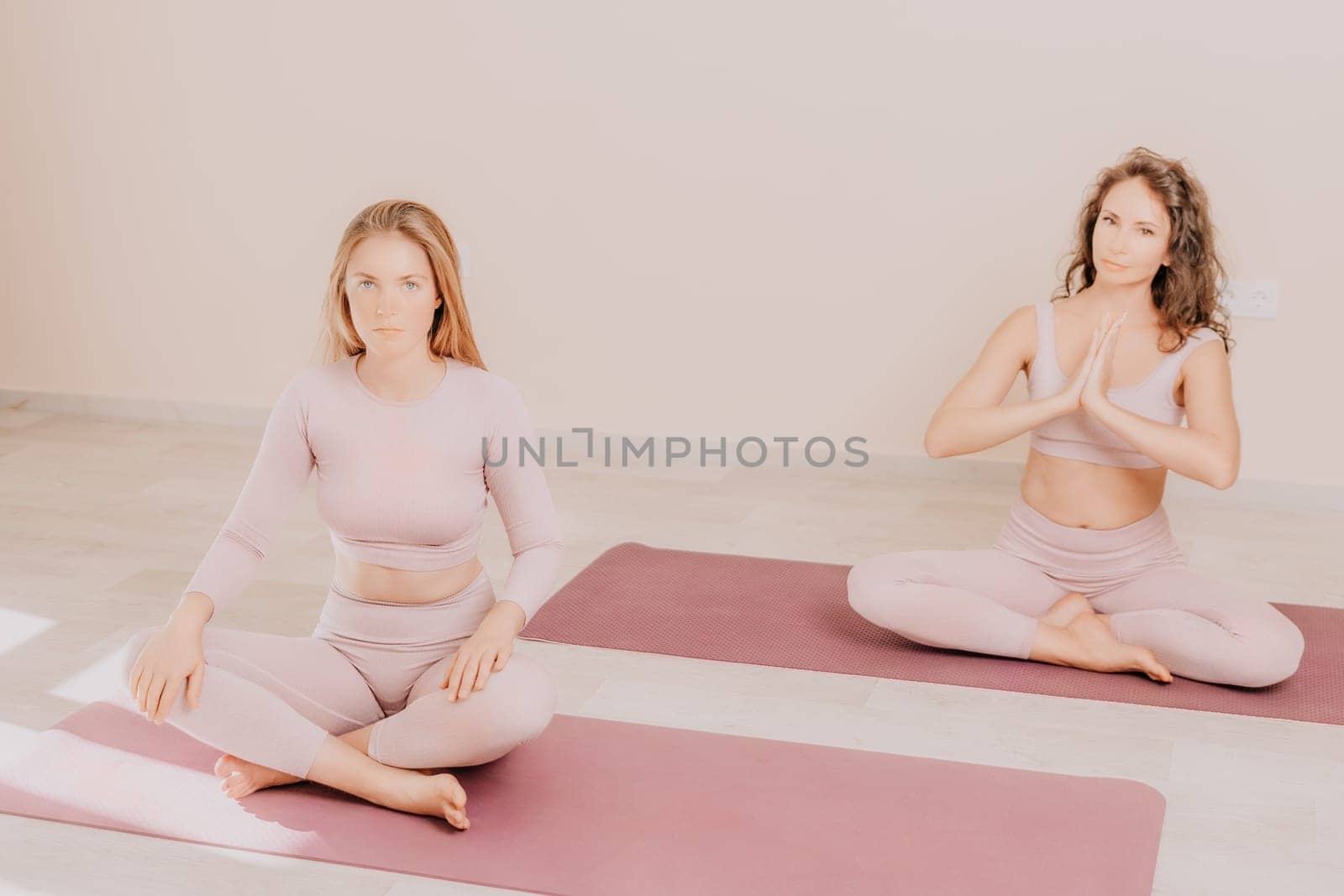 Young woman with long hair in white swimsuit and boho style braclets practicing outdoors on yoga mat by the sea on a sunset. Women's yoga fitness routine. Healthy lifestyle, harmony and meditation