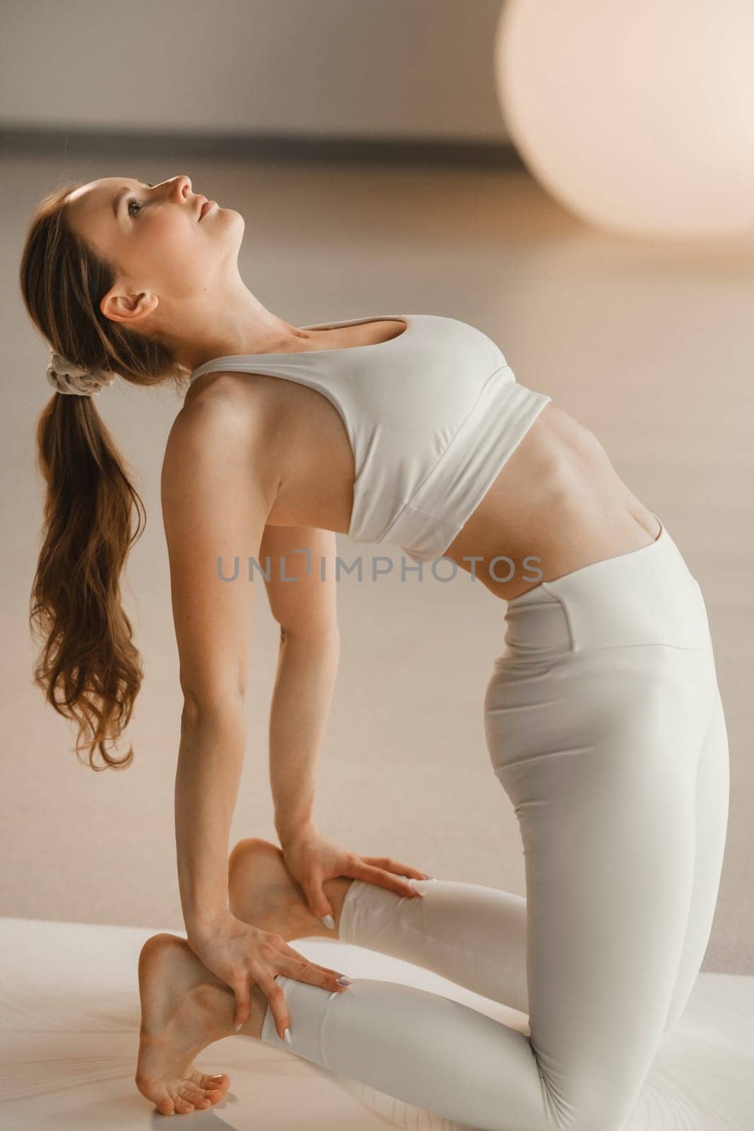 A girl in white clothes does yoga on a mat indoors.