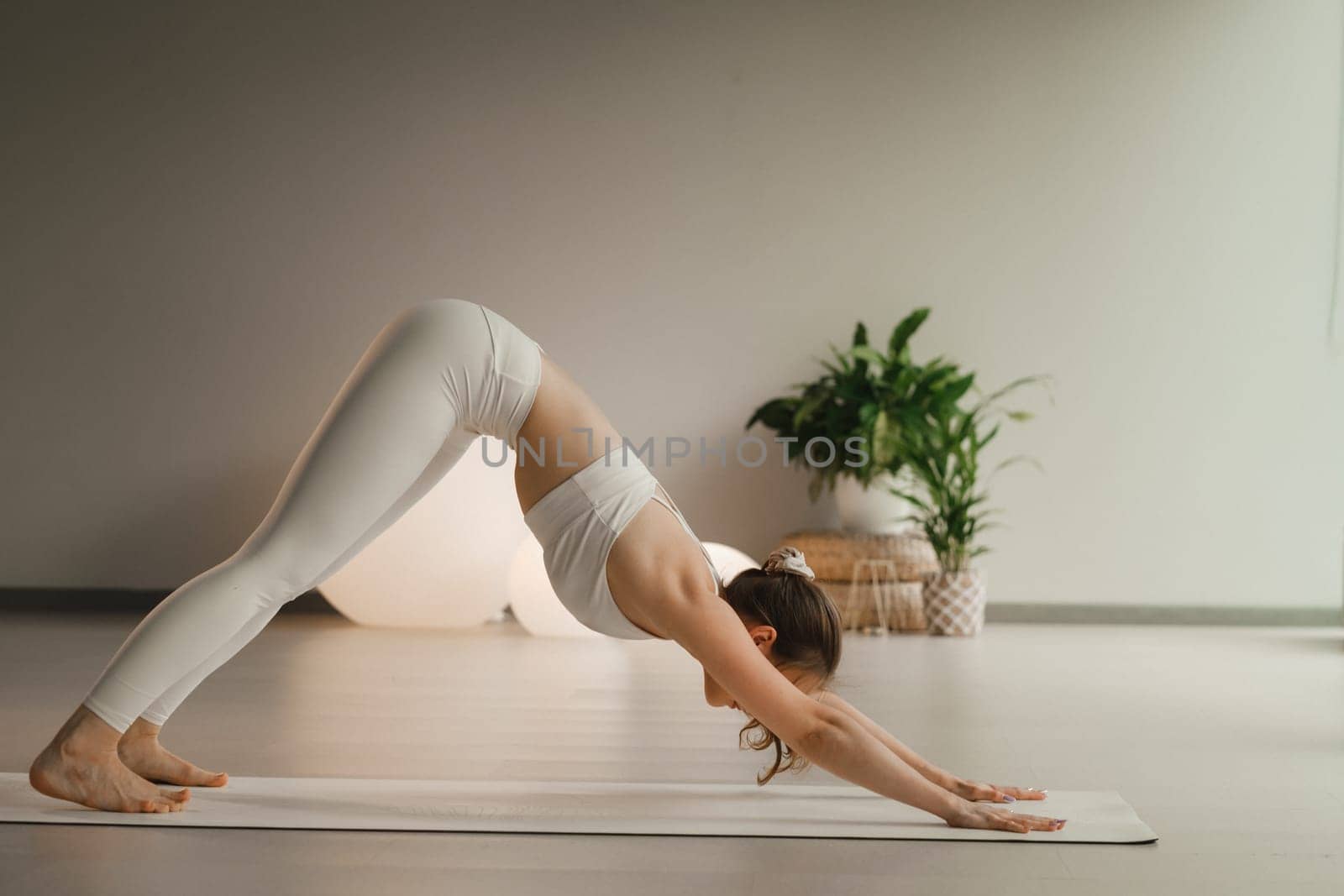 A girl in white clothes does yoga on a mat indoors by Lobachad