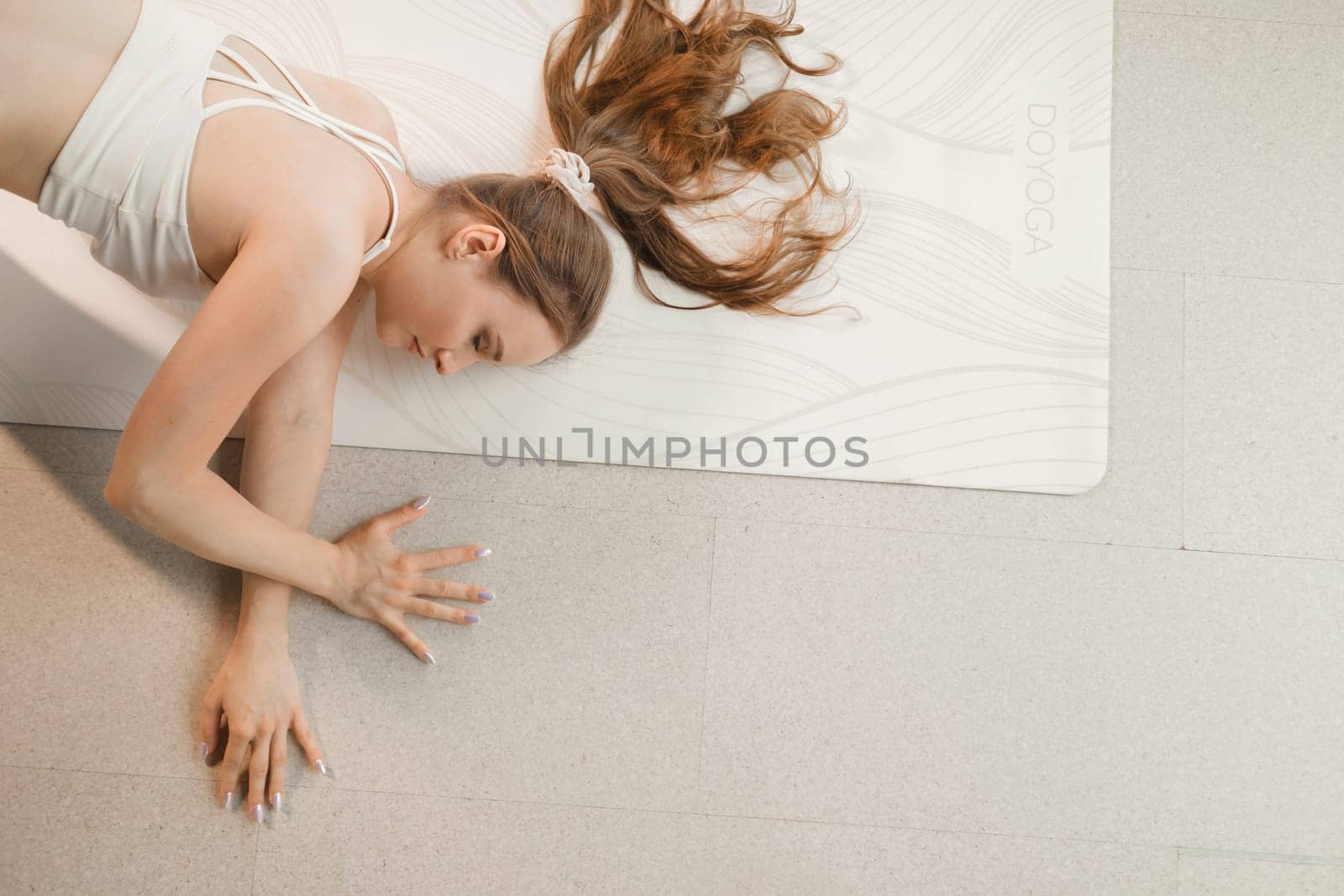 A girl in white clothes does yoga lying on a rug indoors by Lobachad
