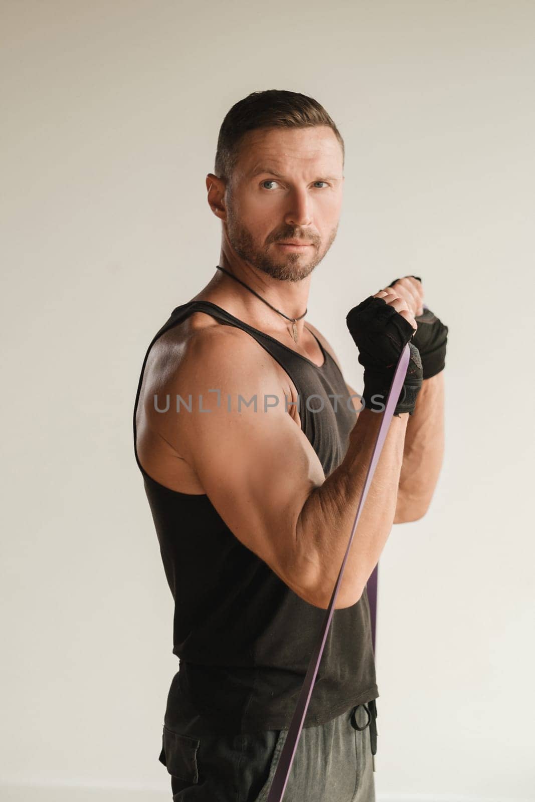 A man in black sportswear is engaged in strength fitness using a rubber loop indoors by Lobachad