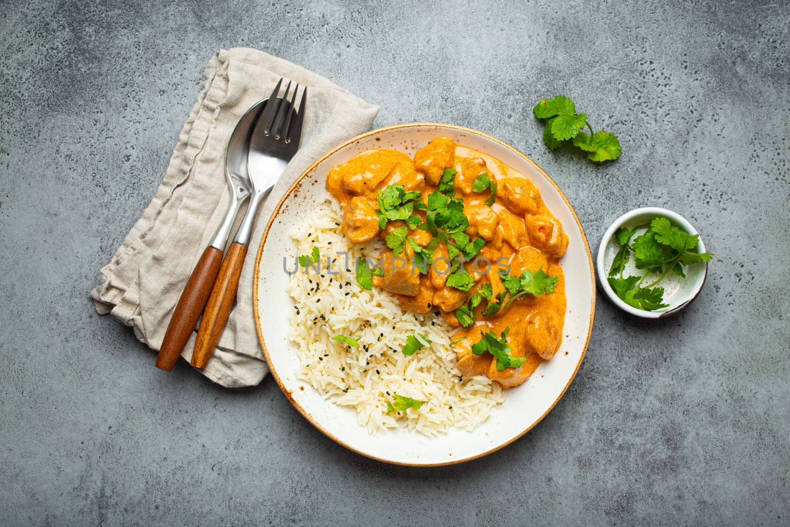 Traditional Indian dish chicken curry with basmati rice and fresh cilantro on rustic white plate on gray concrete table background from above. Indian dinner meal by its_al_dente