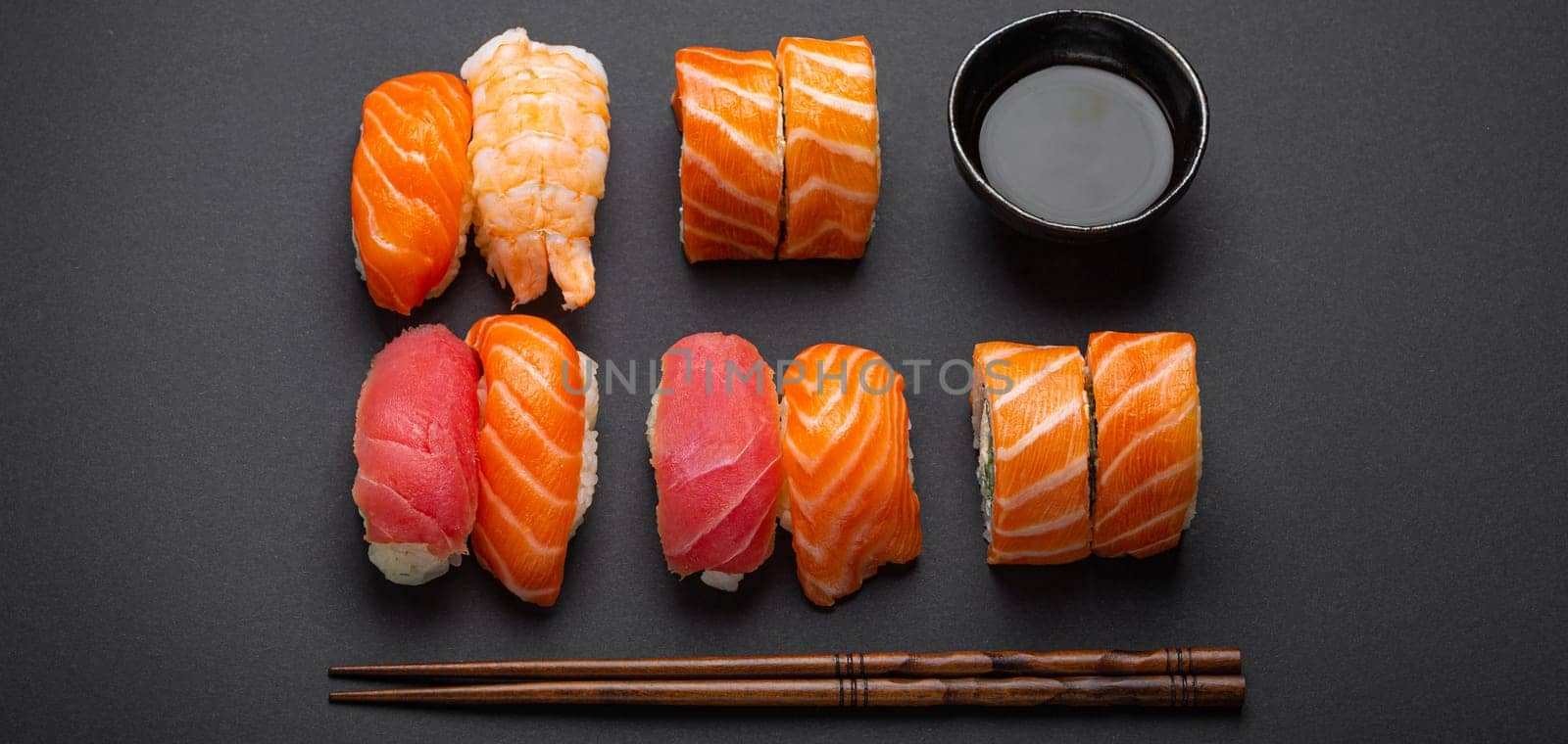 Set of traditional Japanese sushi and rolls top view with soy sauce and chopsticks on dark black minimal background. Sushi with salmon, tuna and shrimp