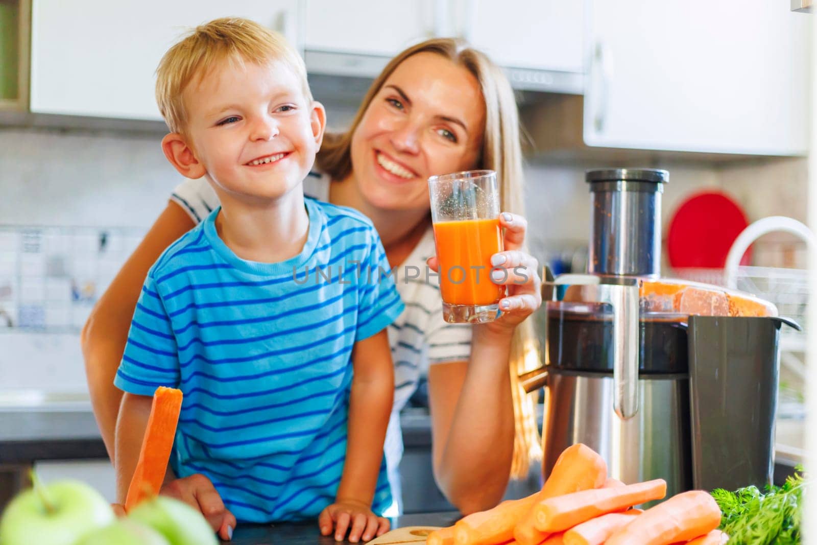 Mom and son drink fresh carrot juice squeezed using a juicer in the kitchen at home. Family nutrition, healthy eating concept