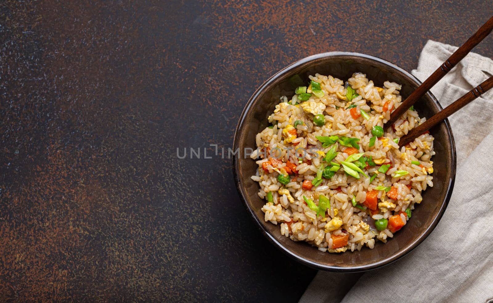 Authentic Chinese and Asian fried rice with egg and vegetables in ceramic brown bowl top view on dark rustic concrete table background. Traditional dish of China with space for text by its_al_dente