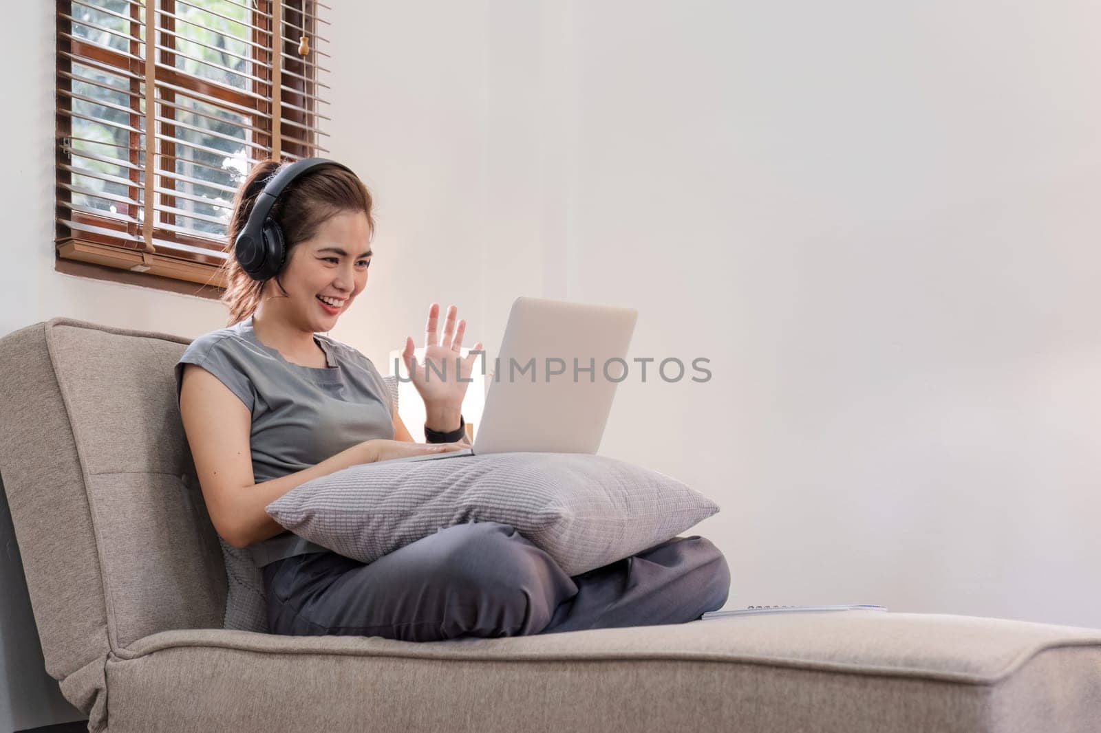 A young woman talks with a friend through a video call program on a laptop in the living room..