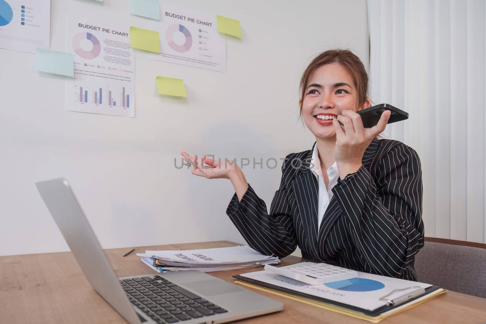 Asian businesswoman in a formal suit in the office is happy and cheerful while using a smartphone to work in her office..