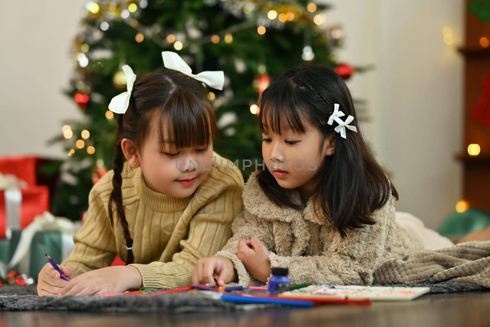 Two little girls making greeting card for New Year and Christmas while lying on floor in living room by prathanchorruangsak