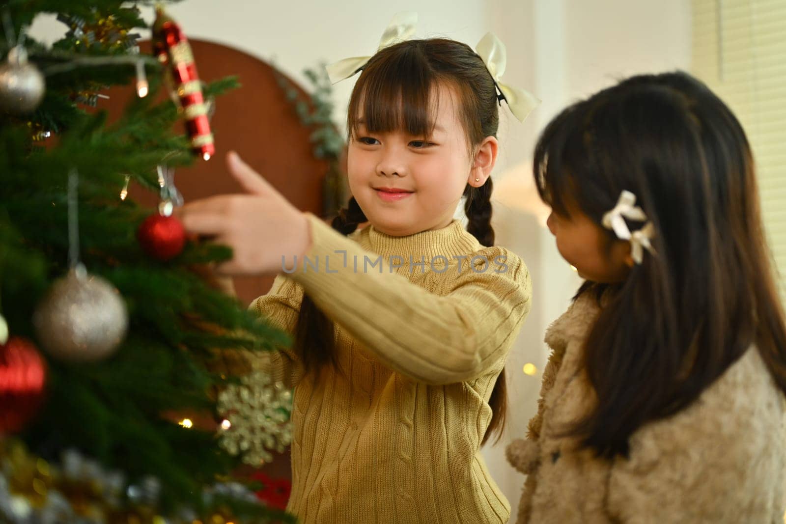 Two happy girls decorating Christmas tree and enjoying preparing winter holidays at home.