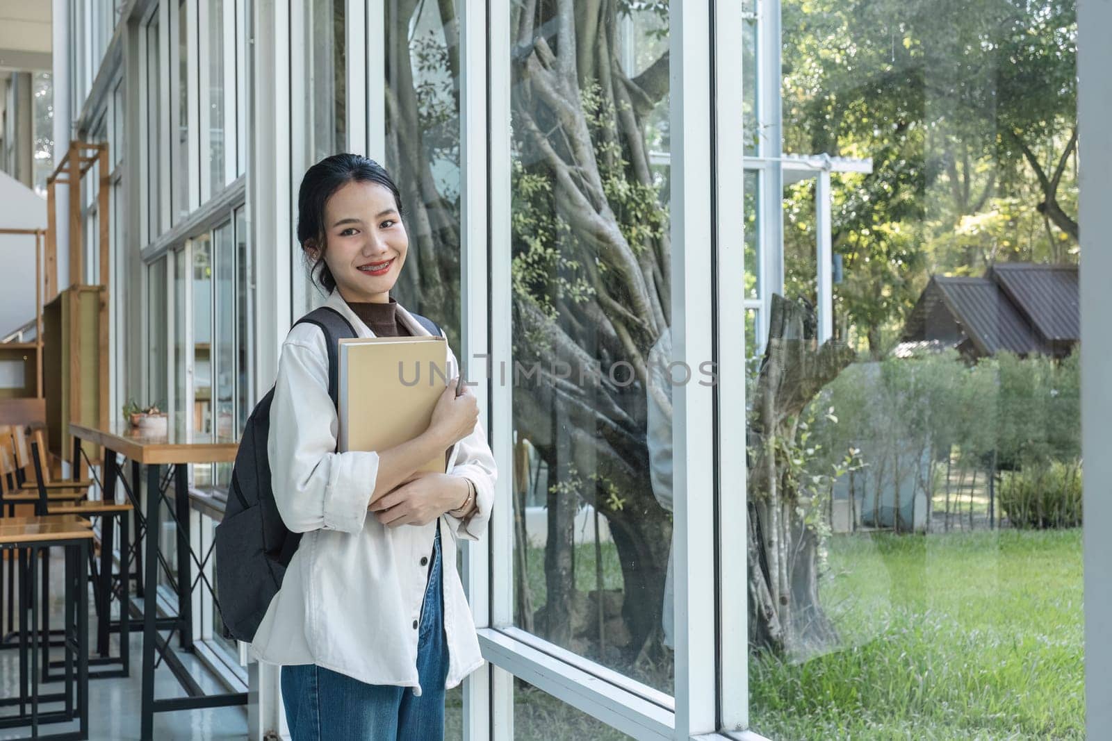 Attractive young Asian female student stands holding a book to make an appointment with a college friend..