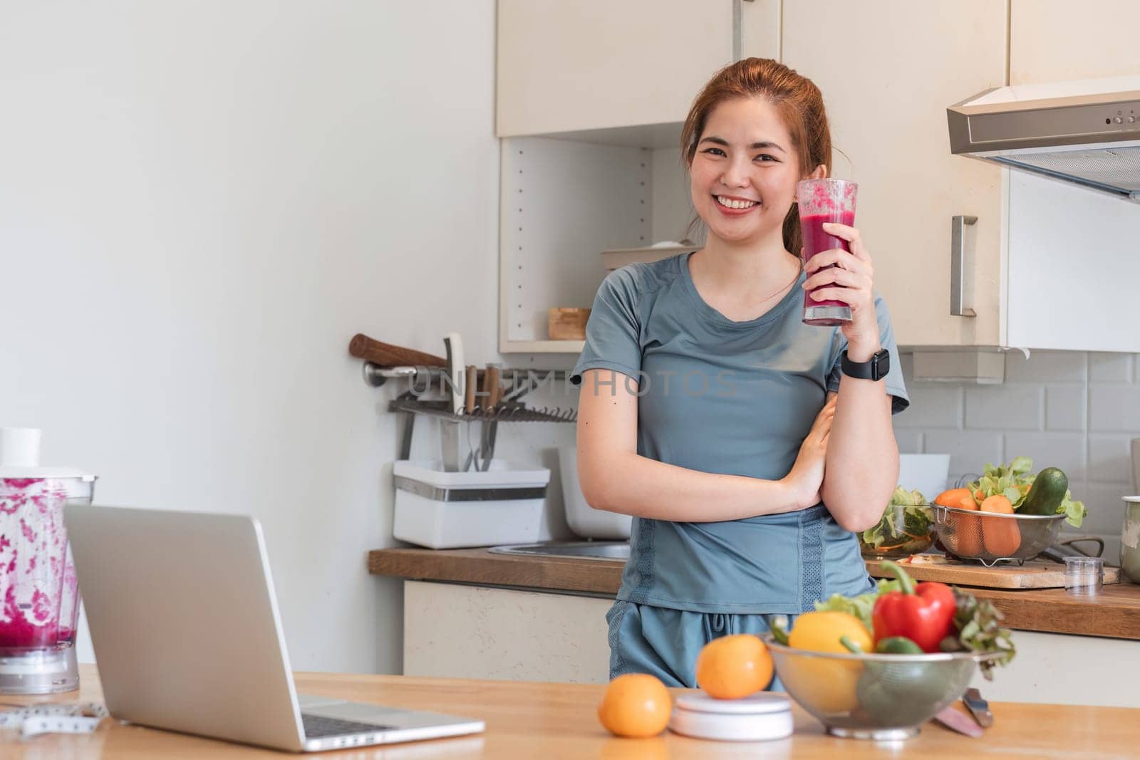 Beautiful young woman in exercise clothes having fun in a cute kitchen at home. Preparing a vegetarian fruit salad or a healthy smoothie..