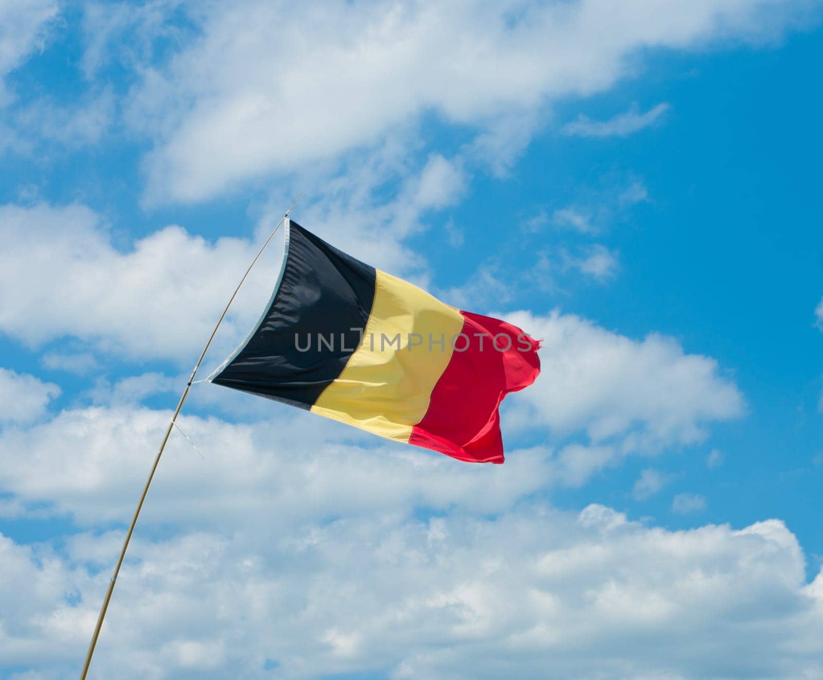 belgian flag in a strong breeze against a blue cloudy sky