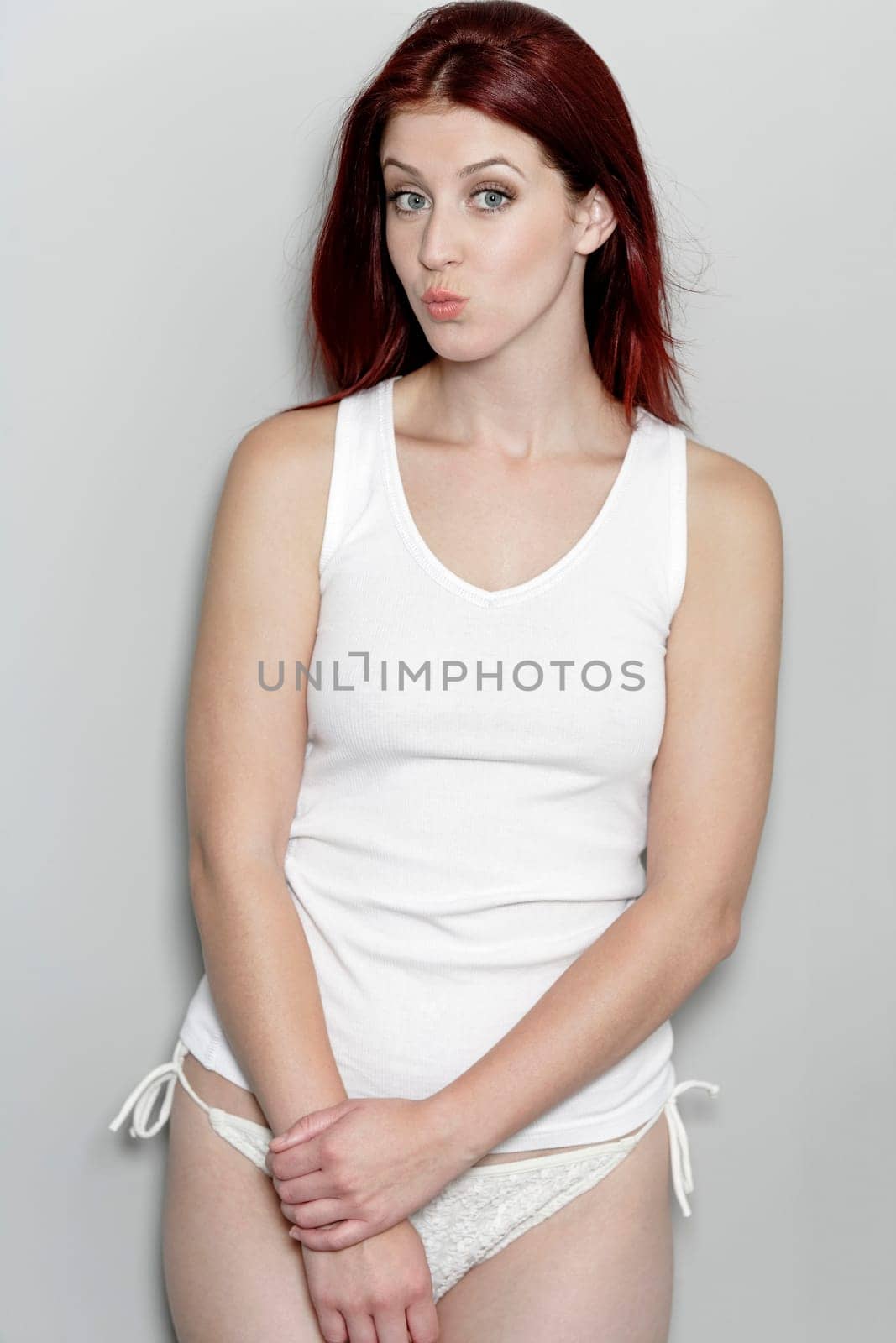 Attractive woman in white bikini bottoms and vest top pulling faces and having fun.