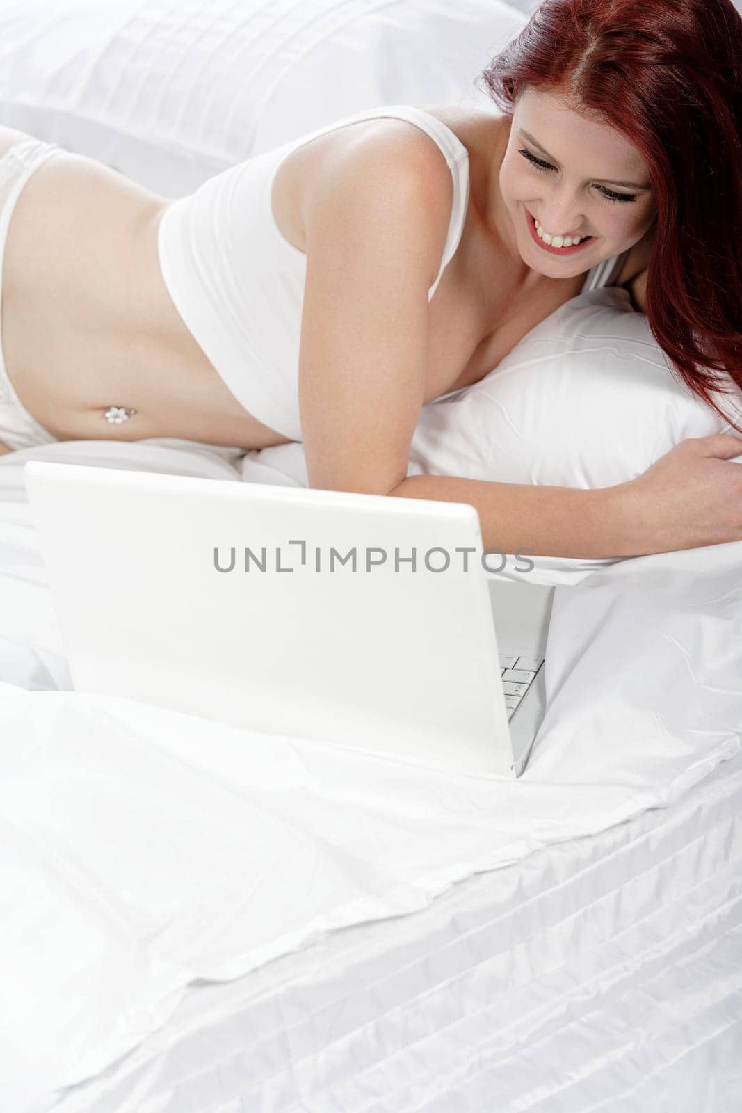 Beautiful young woman using her laptop computer on her bed, while relaxing in her underwear.