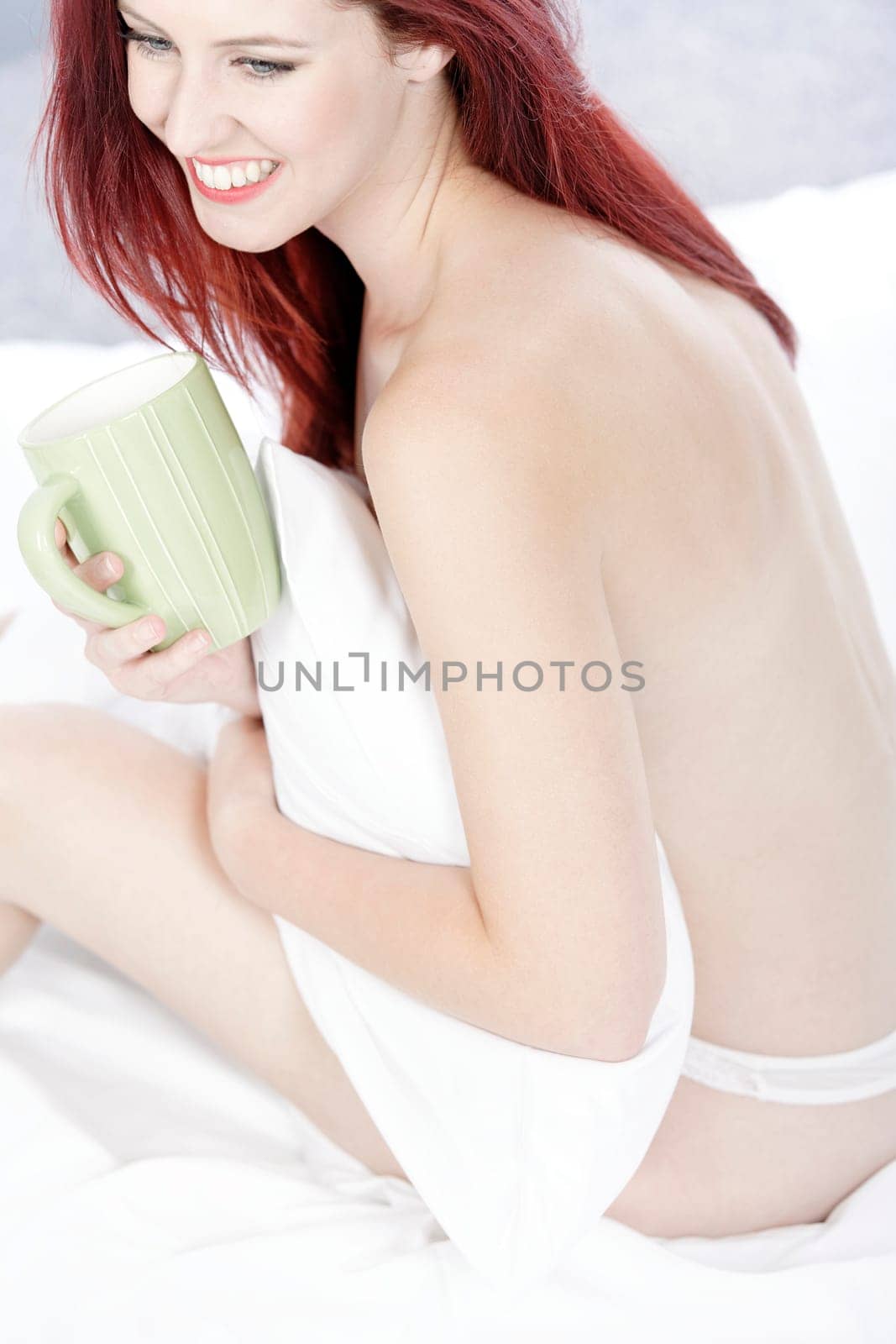 Beautiful young woman naked on her bed at home relaxing on the white covers