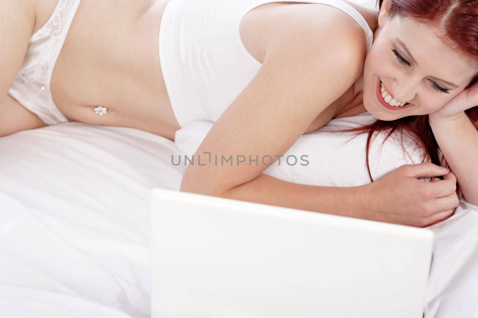 Beautiful young woman using her laptop computer on her bed, while relaxing in her underwear.