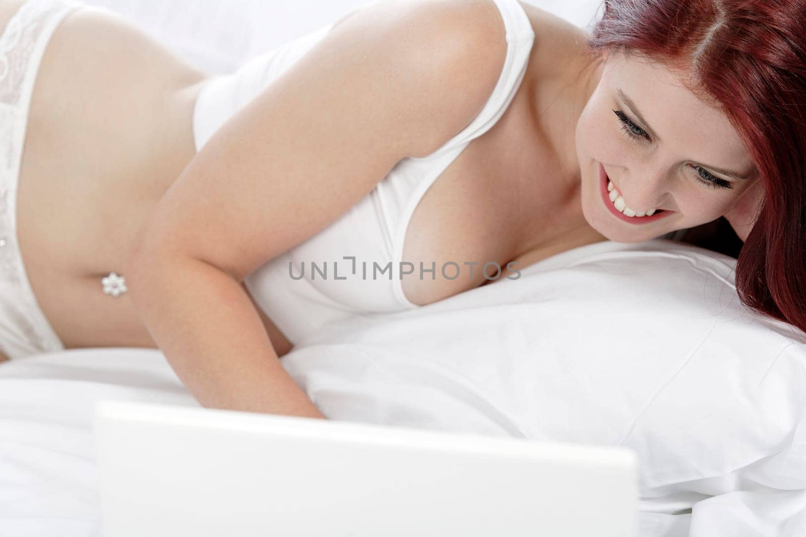 Beautiful young woman using her laptop computer on her bed, while relaxing in her underwear.