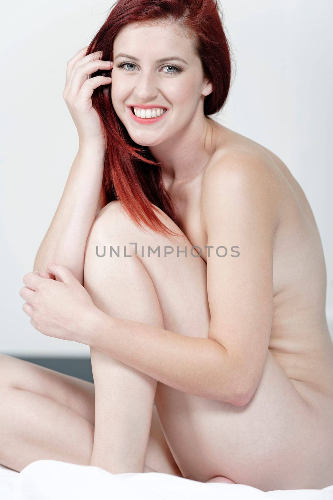 Beautiful young woman naked on her bed at home relaxing on the white covers