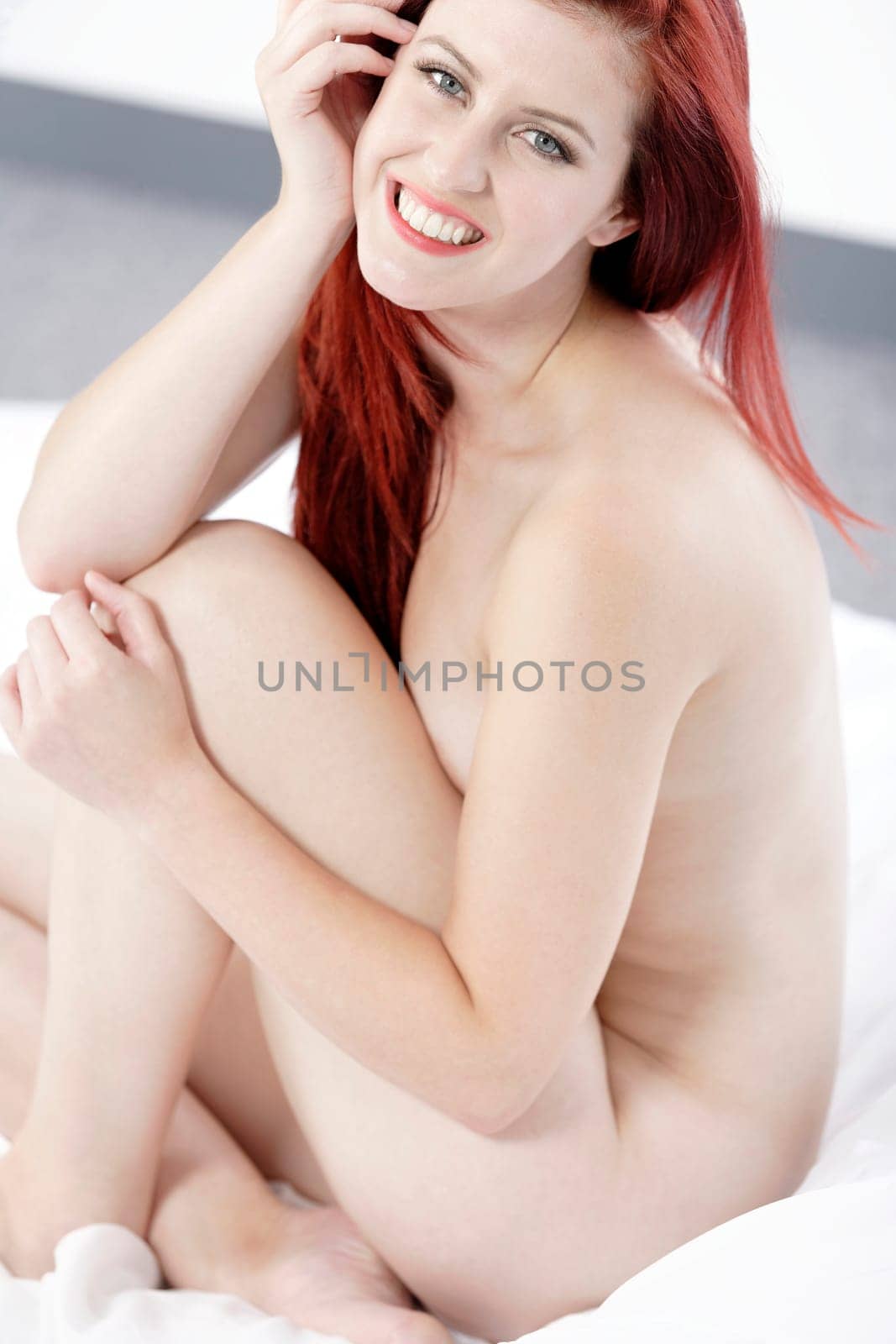 Beautiful young woman naked on her bed at home relaxing on the white covers
