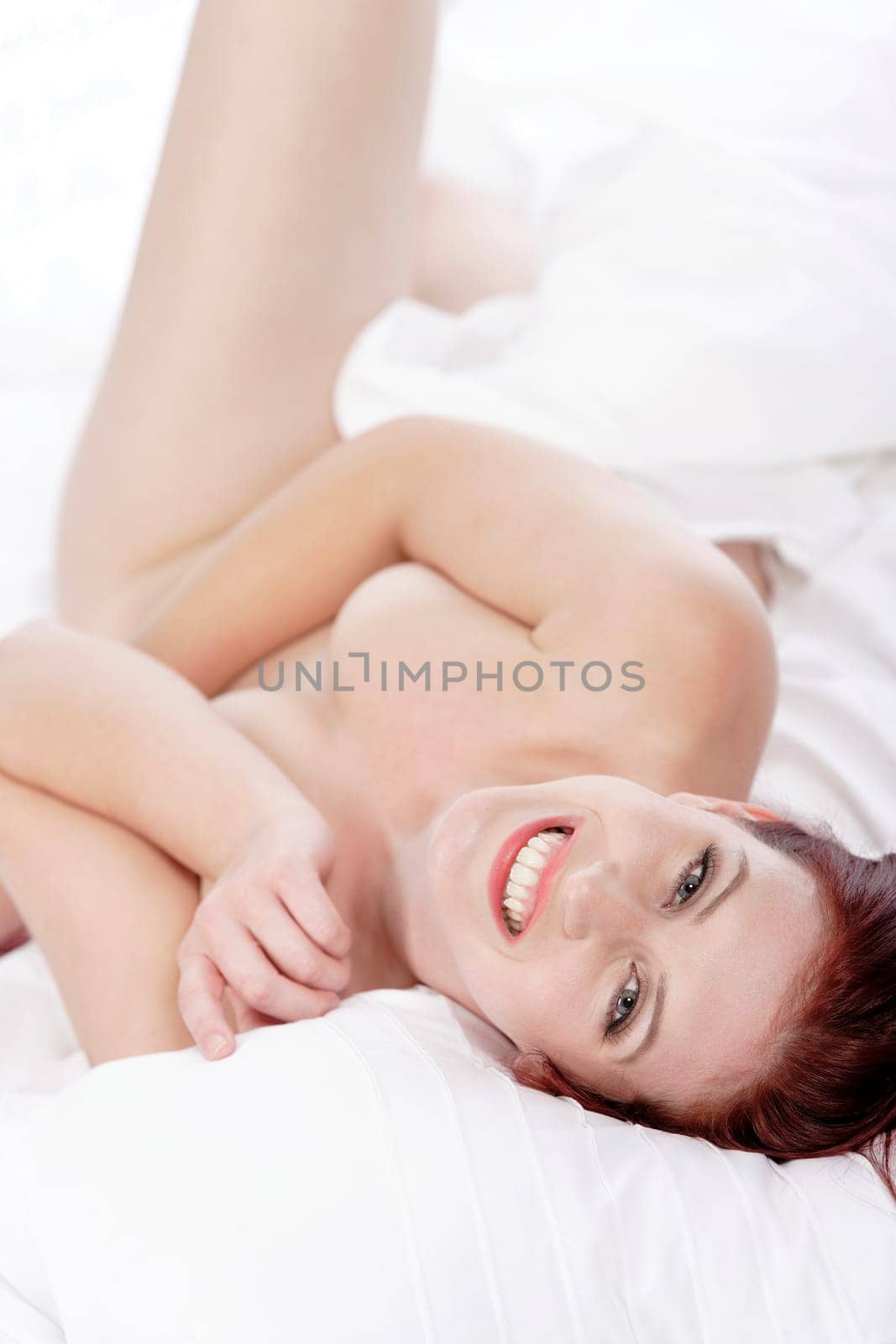 Beautiful young woman naked on her bed at home relaxing on the white covers