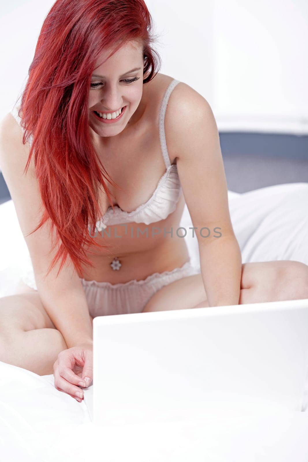 Attractive young woman working on her laptop in white underwear on her bed at home