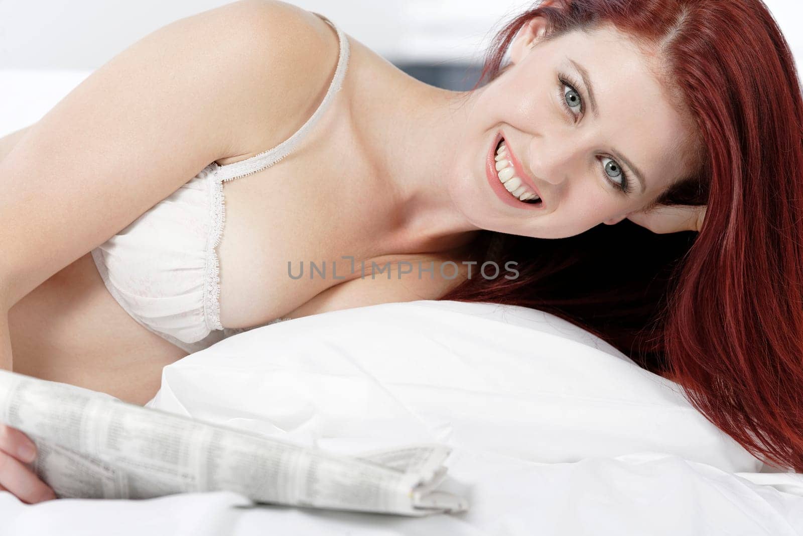 Beautiful young woman in white underwear reading a paper on her bed at home