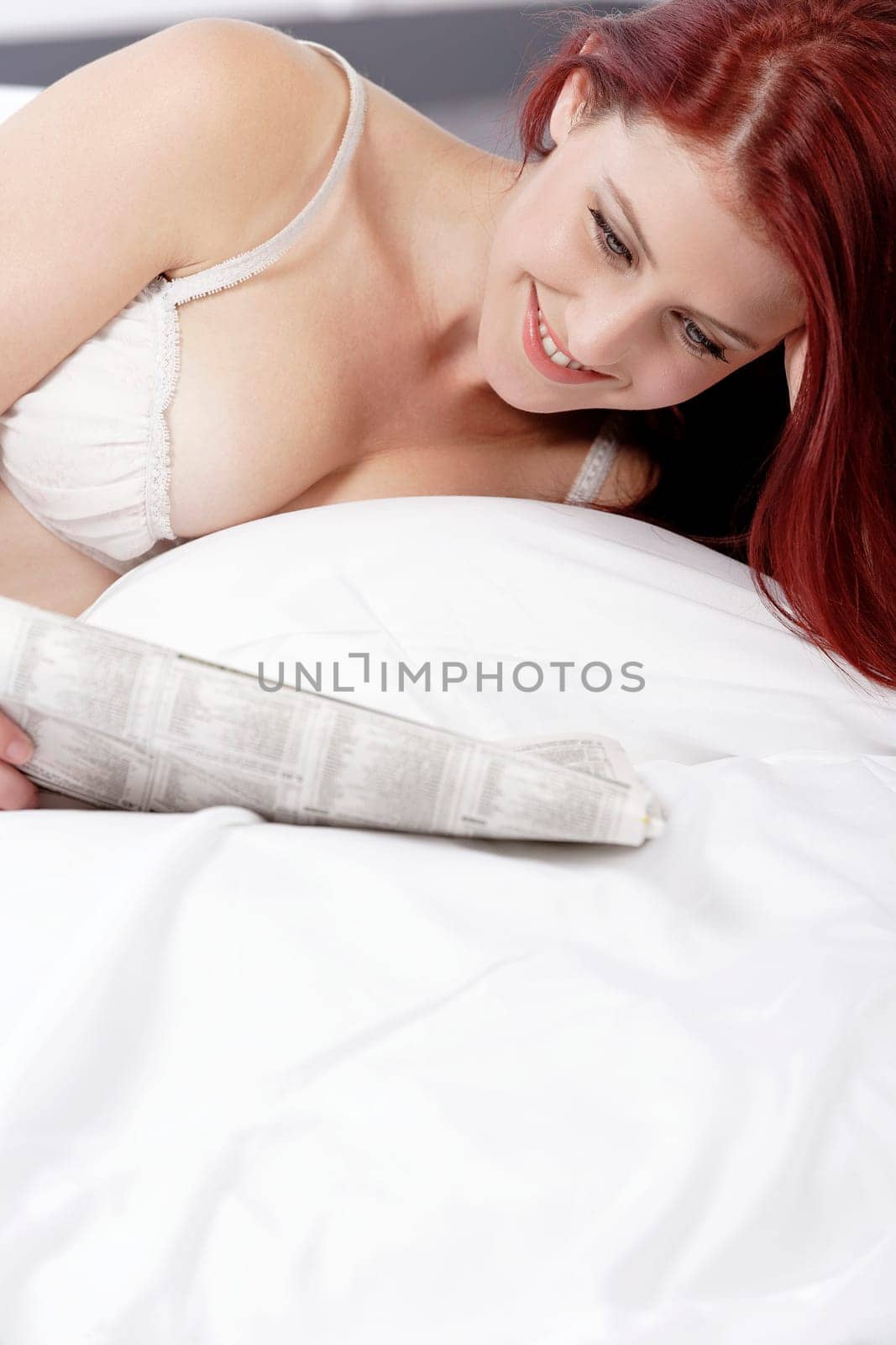 Beautiful young woman in white underwear reading a paper on her bed at home
