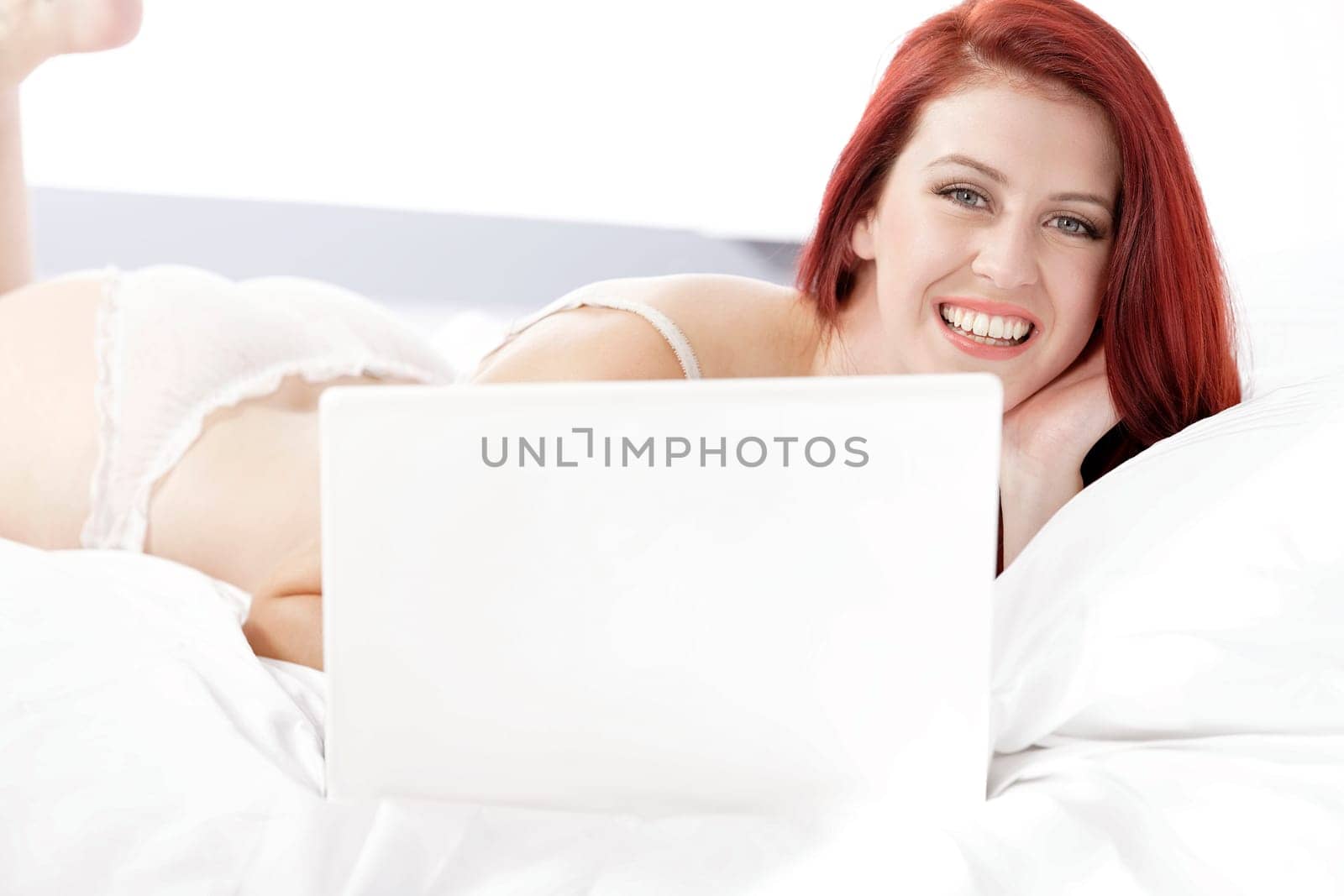 Attractive young woman working on her laptop in white underwear on her bed at home
