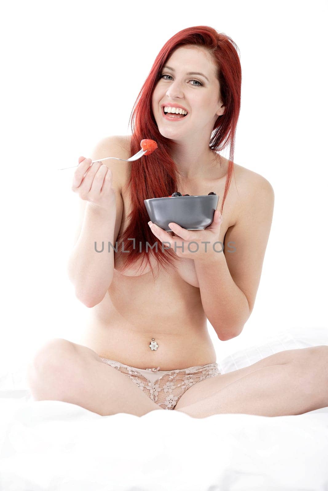 Attractive young woman on her bed at home eating fresh fruit for breakfast