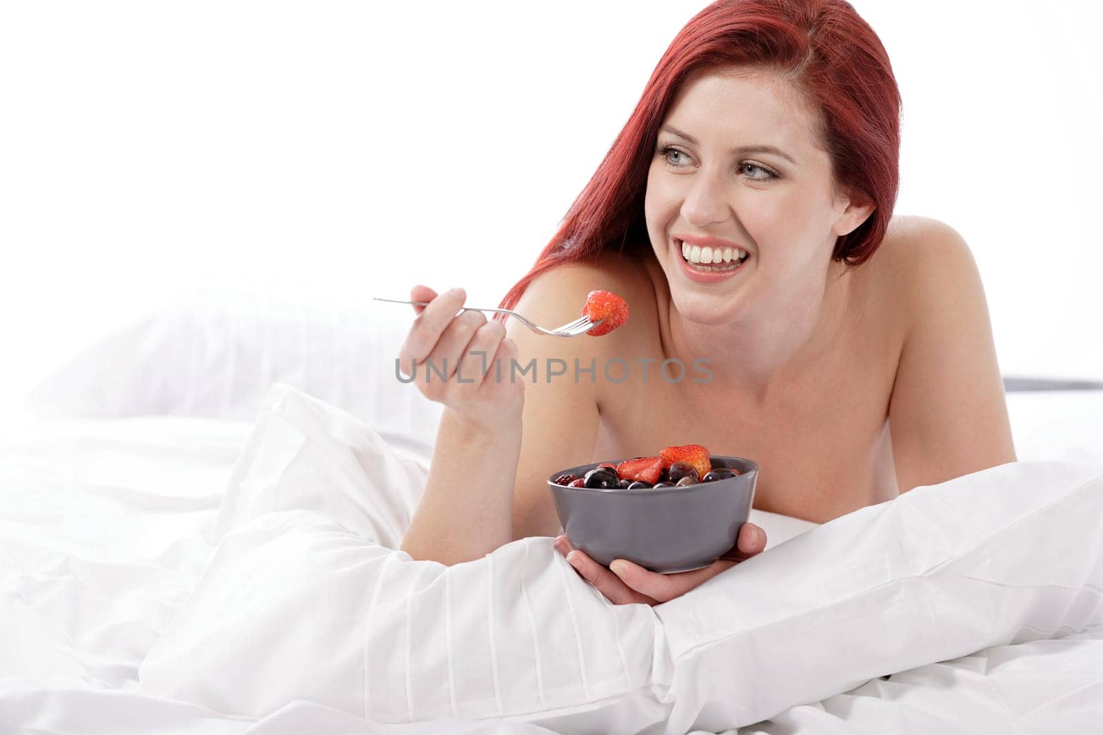 Attractive young woman on her bed at home eating fresh fruit for breakfast