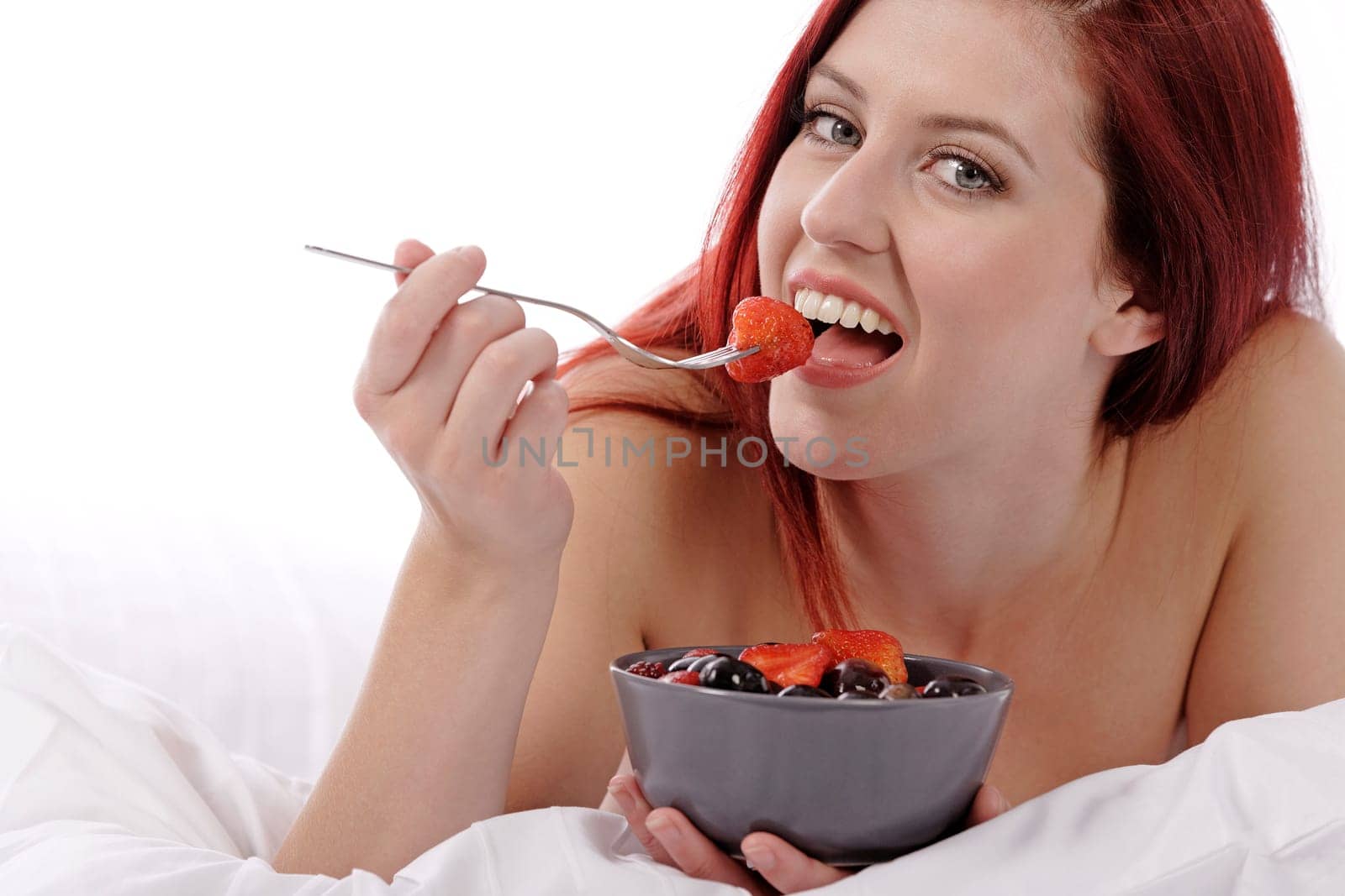 Attractive young woman on her bed at home eating fresh fruit for breakfast