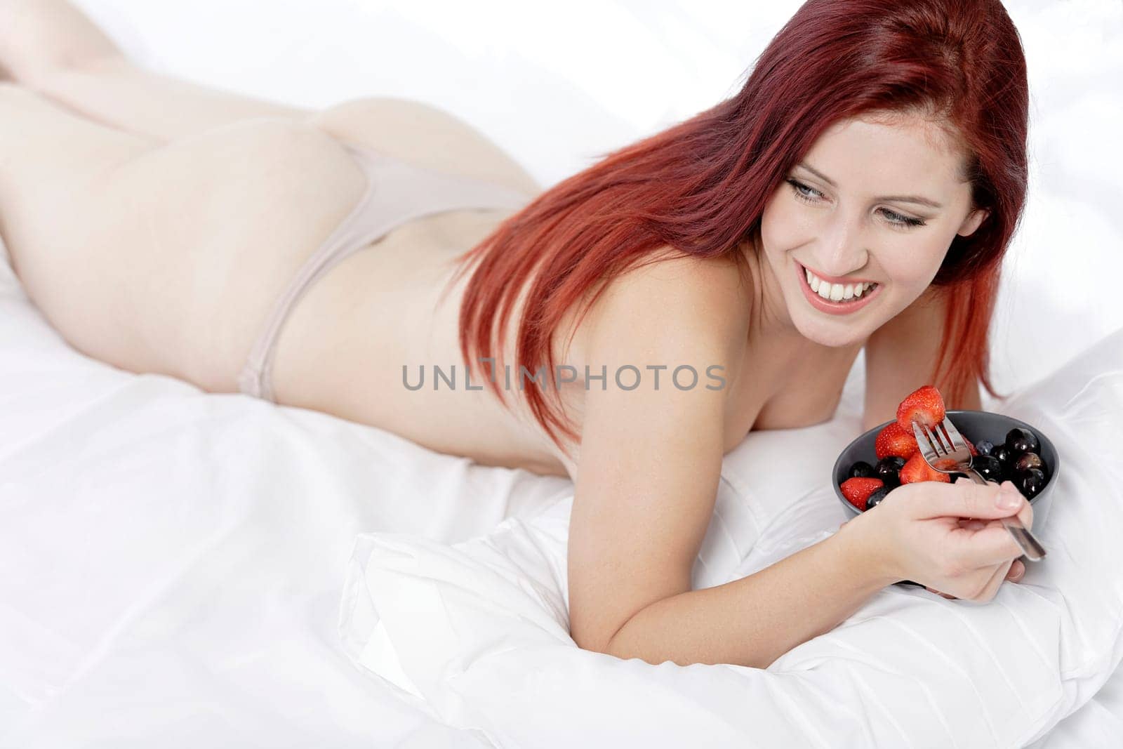 Attractive young woman on her bed at home eating fresh fruit for breakfast