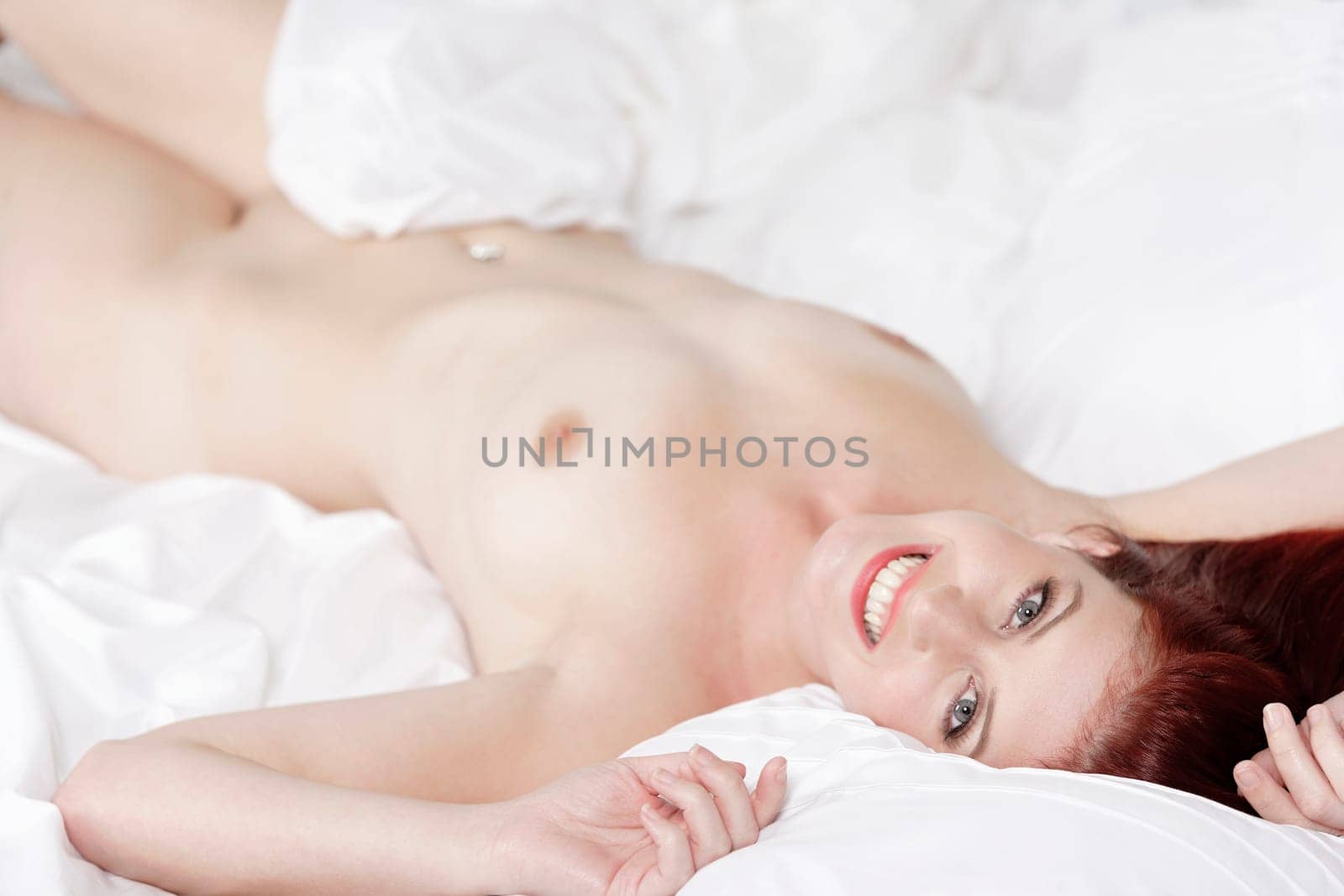 Beautiful young woman naked on her bed at home relaxing on the white covers