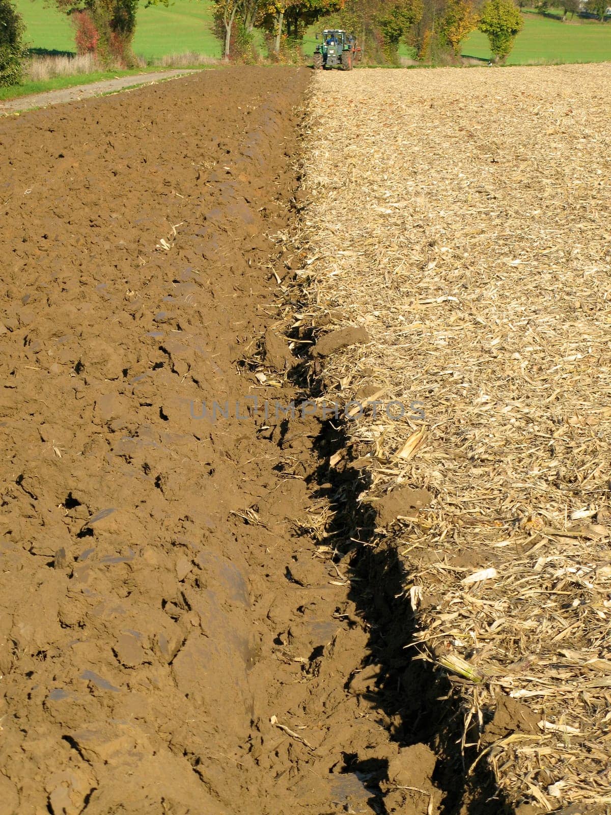 Half-ploughed,brown field in the Kraichgau,Germany. Small green tractor in the background. Portrait